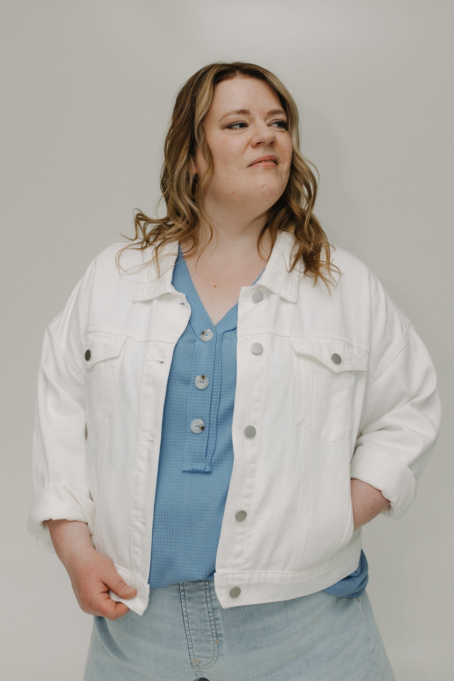 Woman wearing a white denim jacket over a blue shirt on a plain background