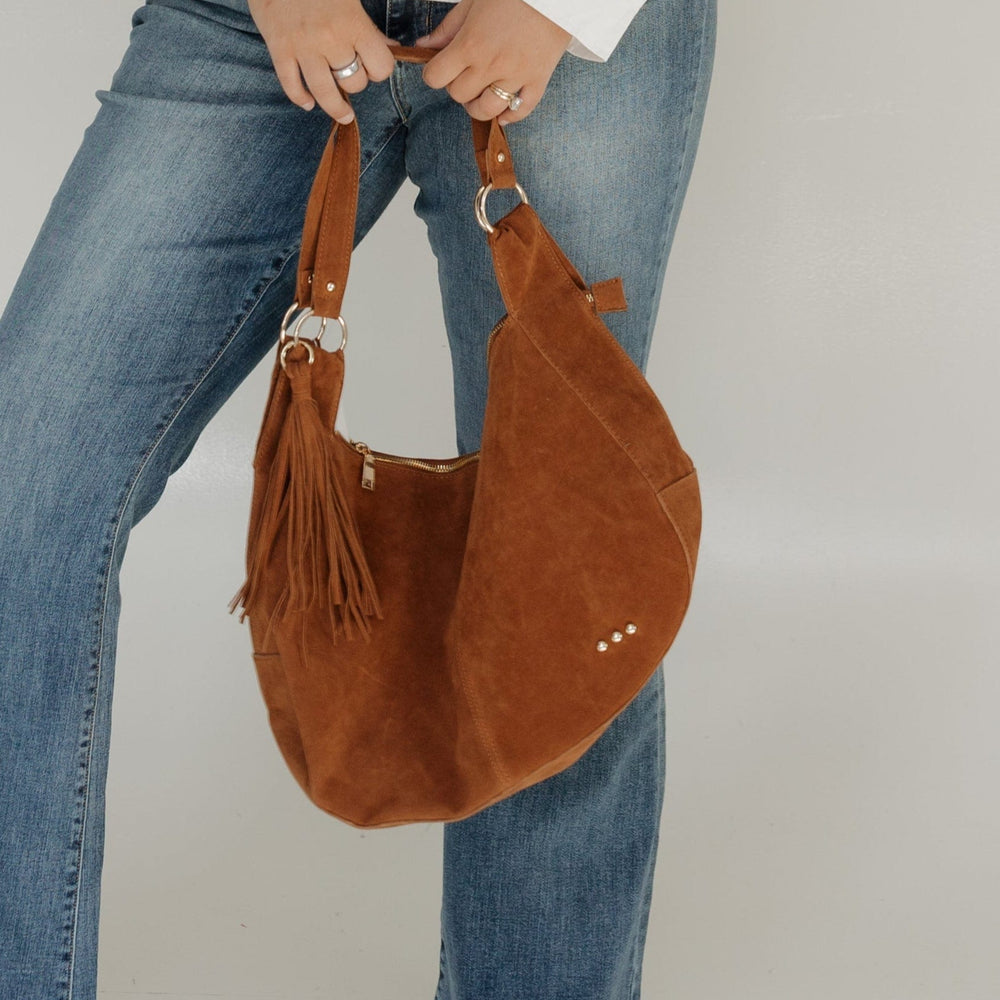 Woman wearing a white sweater, blue jeans, and holding a brown bag against a white background