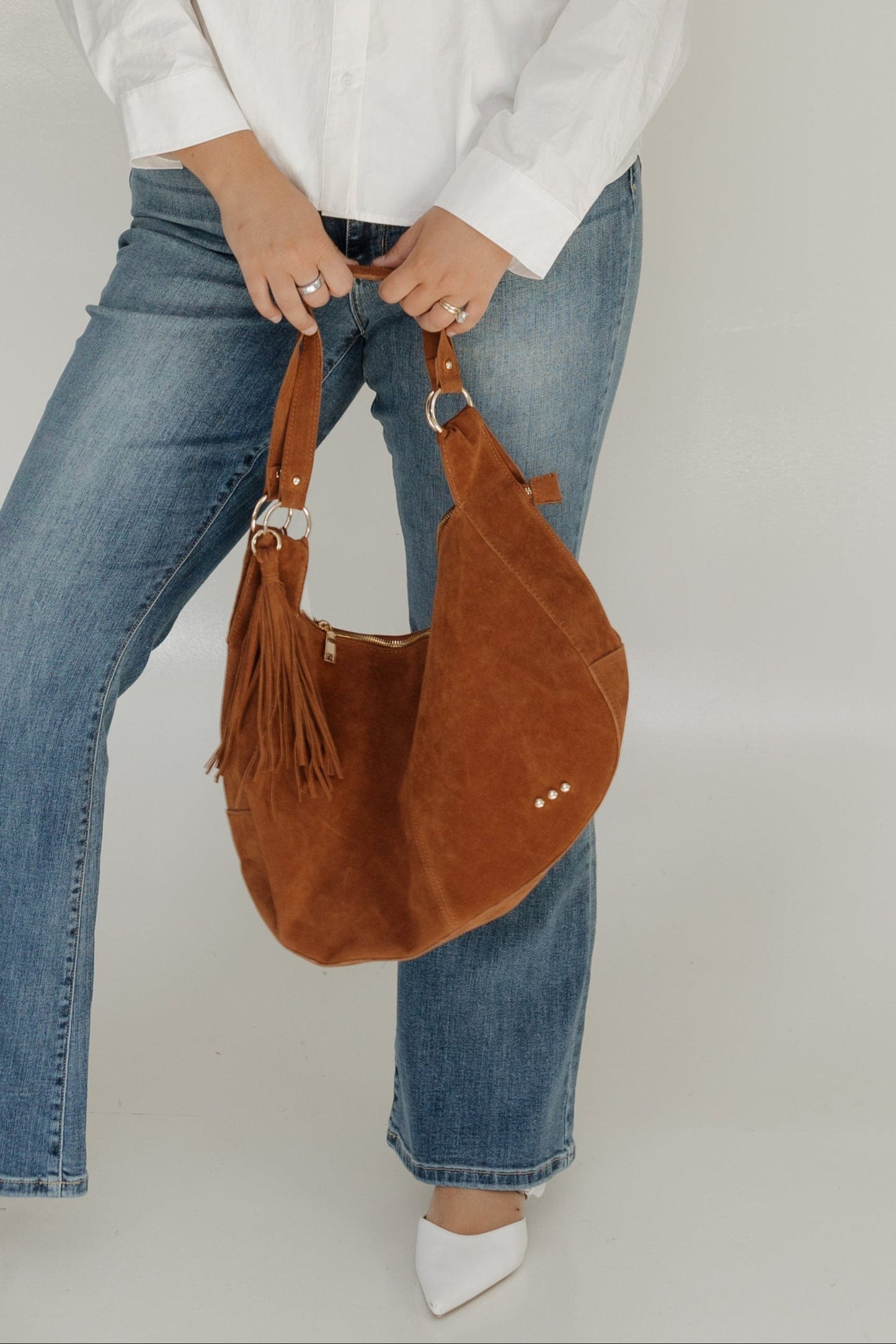 Woman wearing a white sweater, blue jeans, and holding a brown bag against a white background