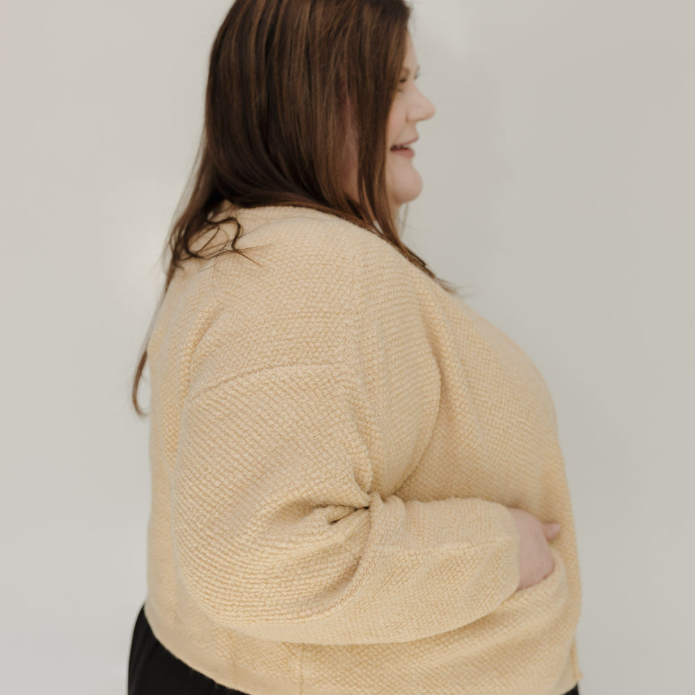 Woman wearing a beige sweater and black pants against a white background