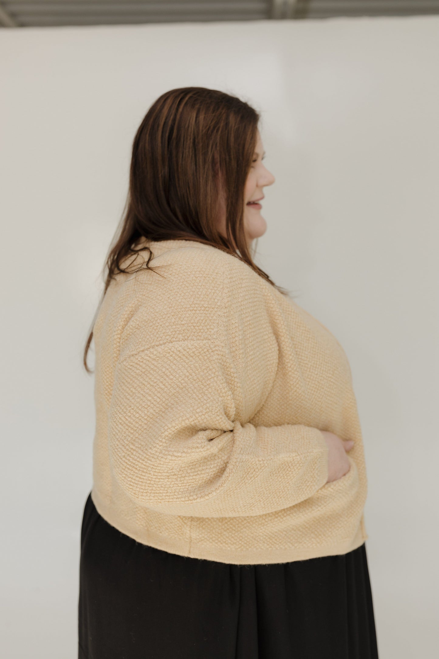 Woman wearing a beige sweater and black pants against a white background