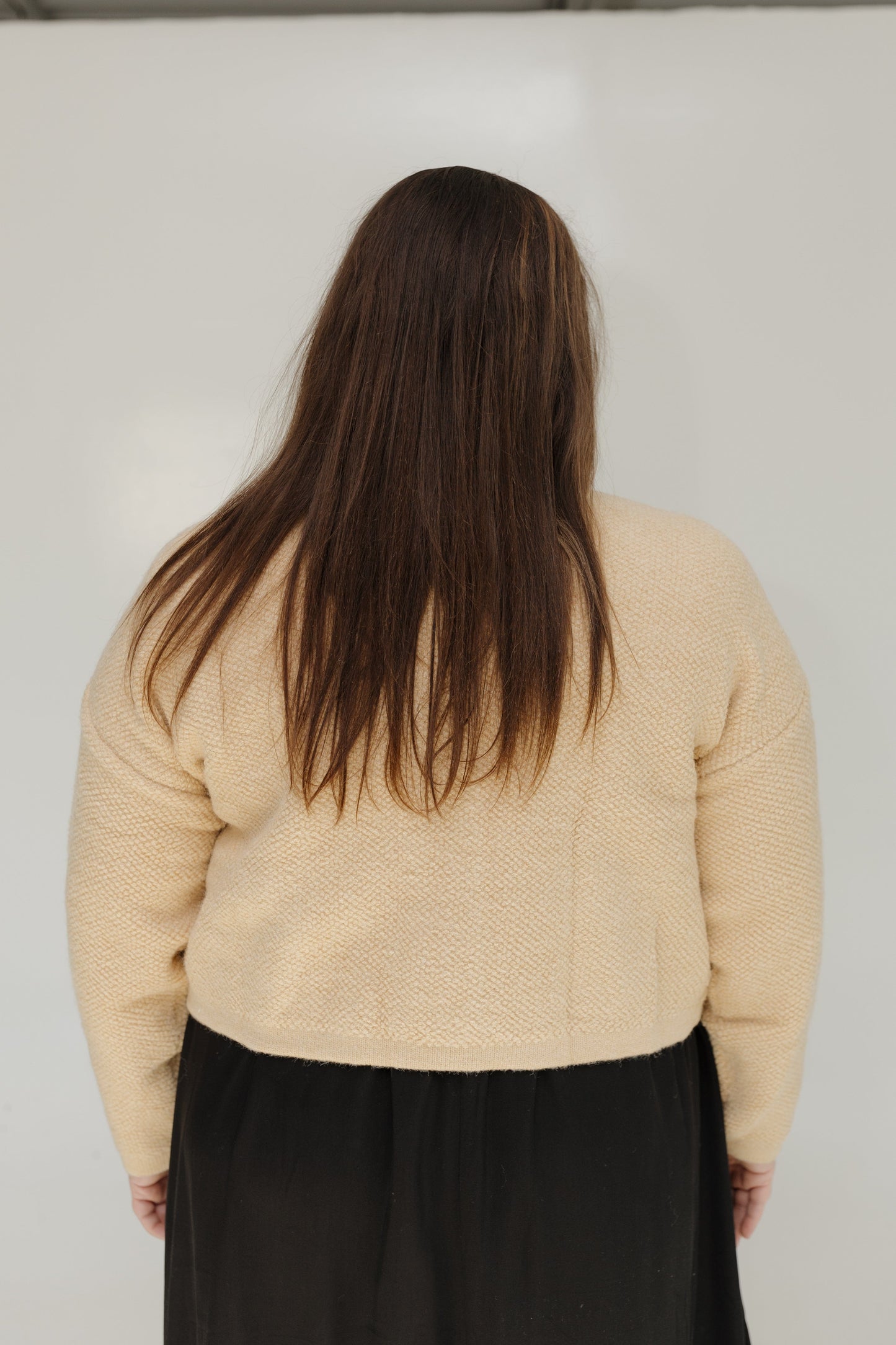 Person wearing a beige sweater and black skirt against a white background