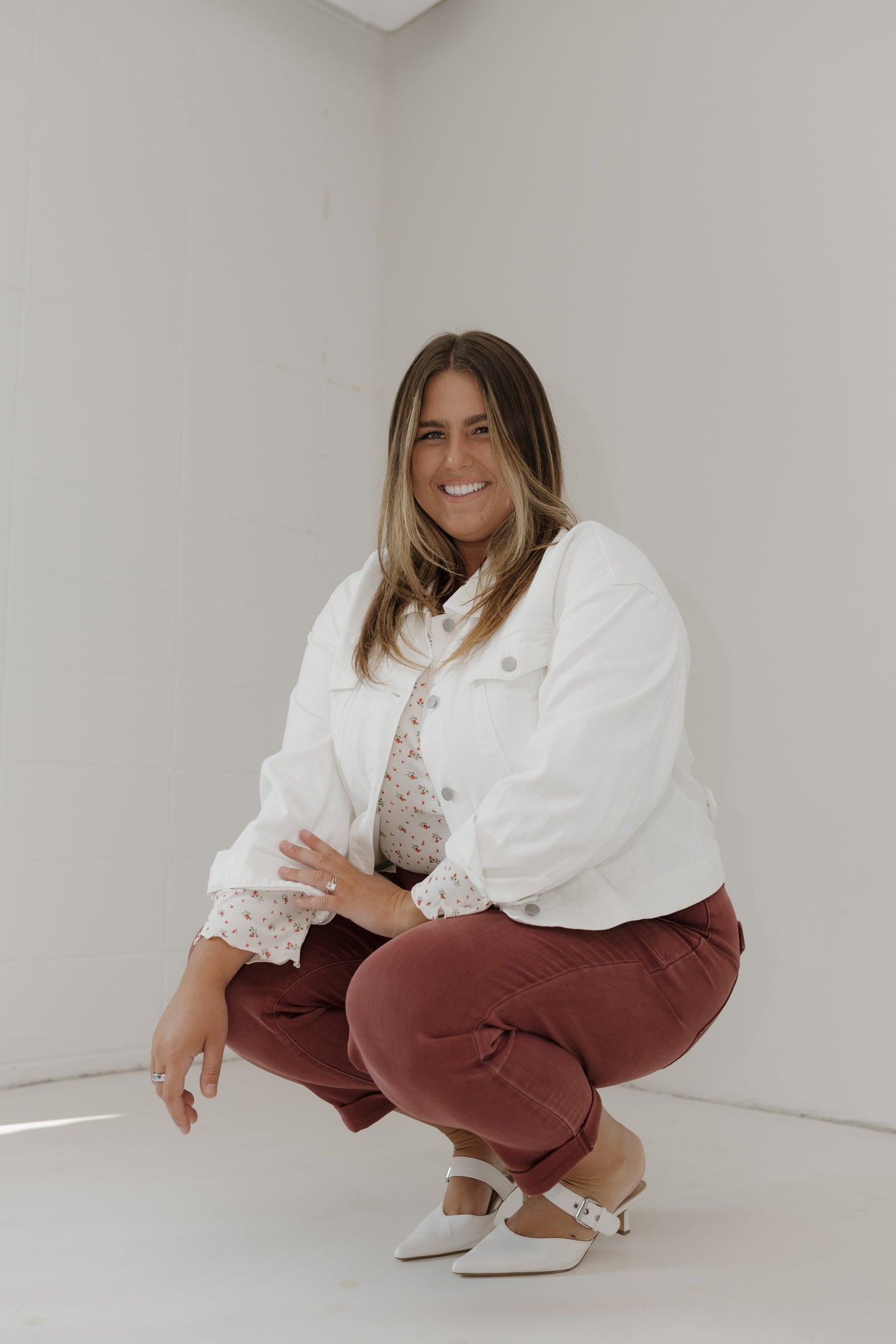 Woman in a white jacket and maroon pants posing against a plain background