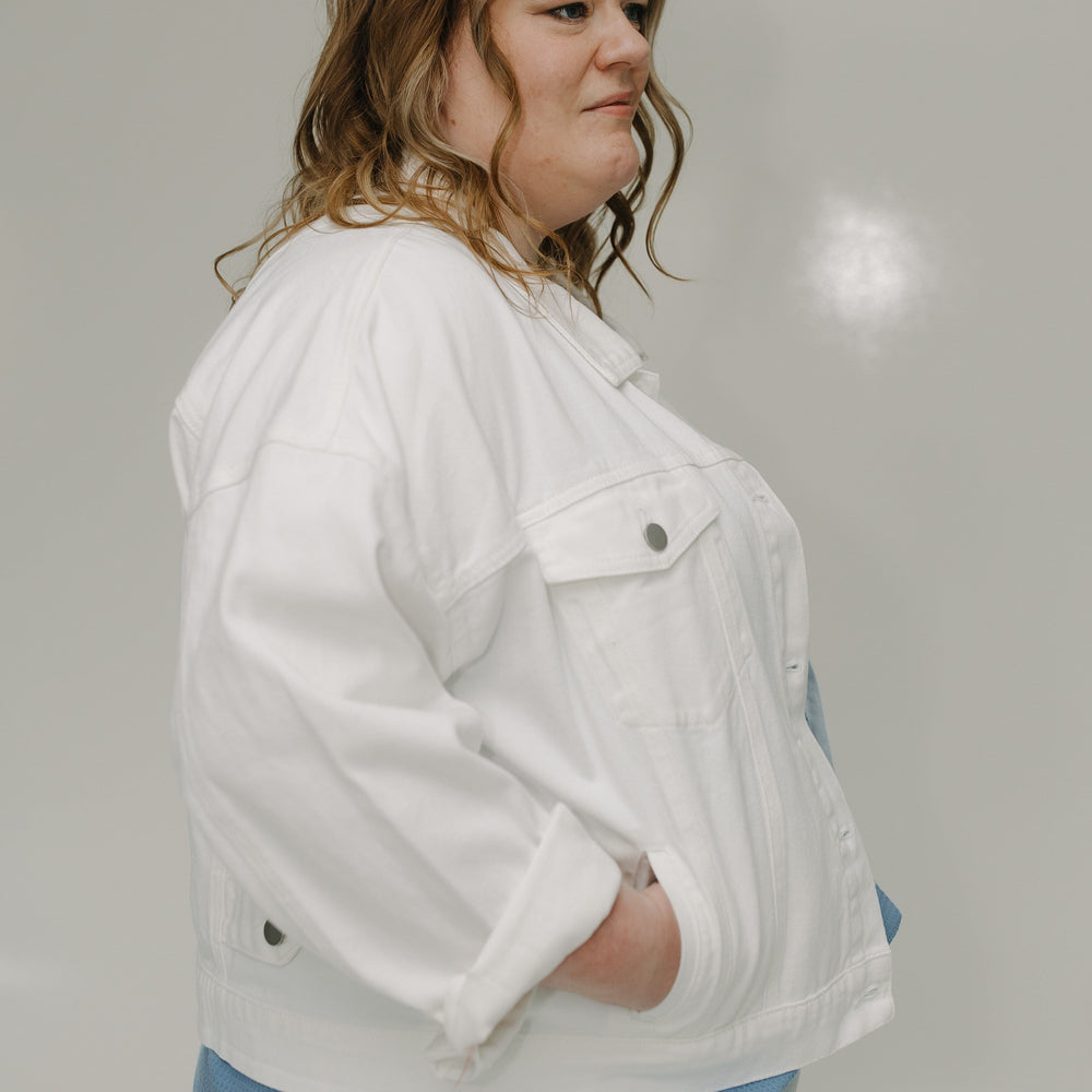 Woman wearing a white jacket over a blue shirt against a plain background