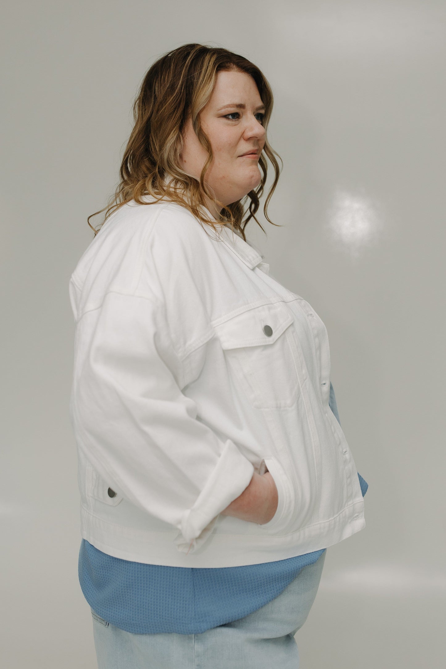 Woman wearing a white jacket over a blue shirt against a plain background