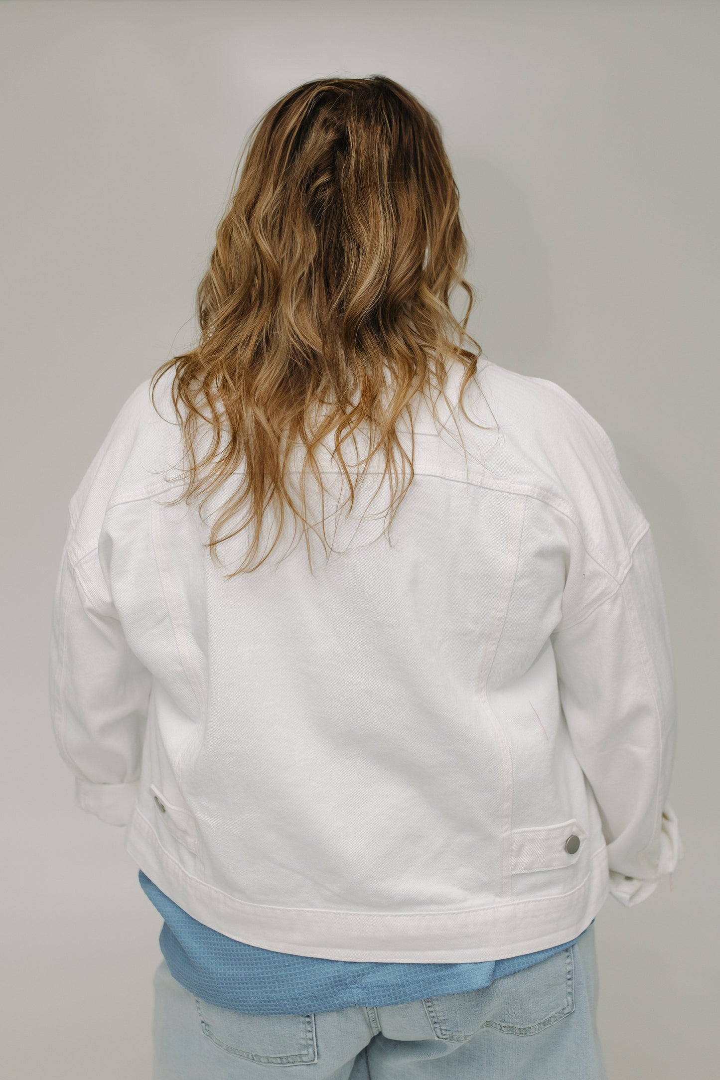 Person wearing a white jacket and light blue jeans against a plain background