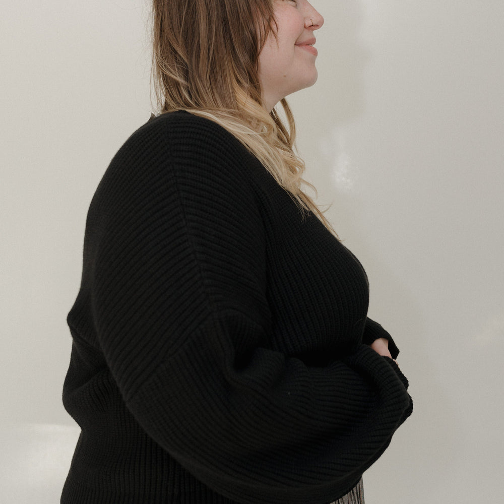 Person wearing a black sweater and pleated skirt against a plain background