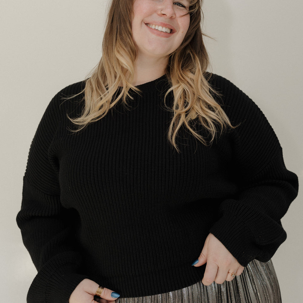 Person wearing a black sweater and pleated skirt against a plain background