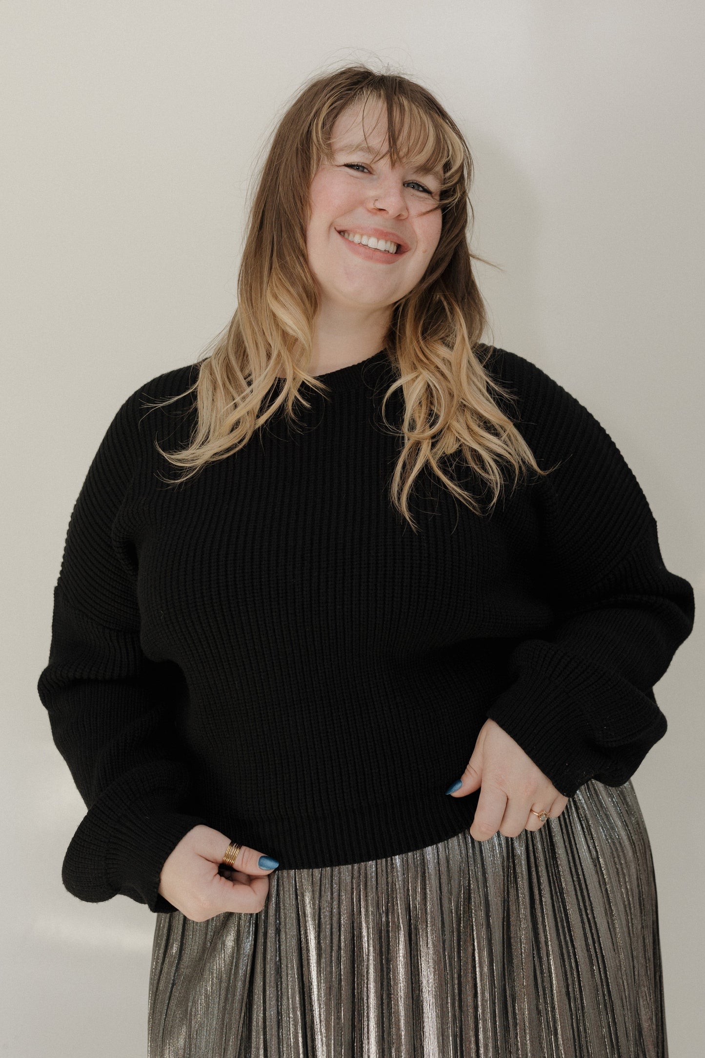 Person wearing a black sweater and pleated skirt against a plain background