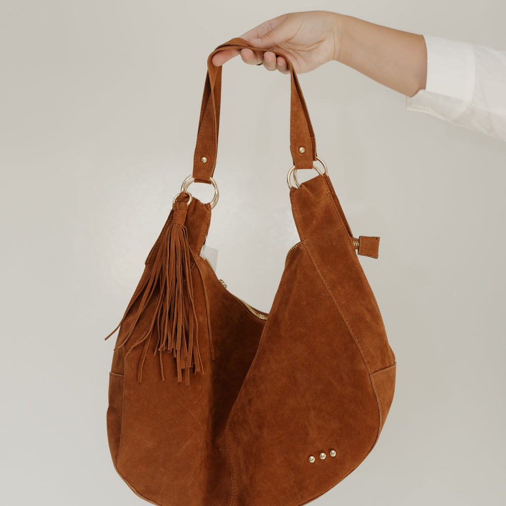 Brown suede handbag with tassels held by a person against a white background