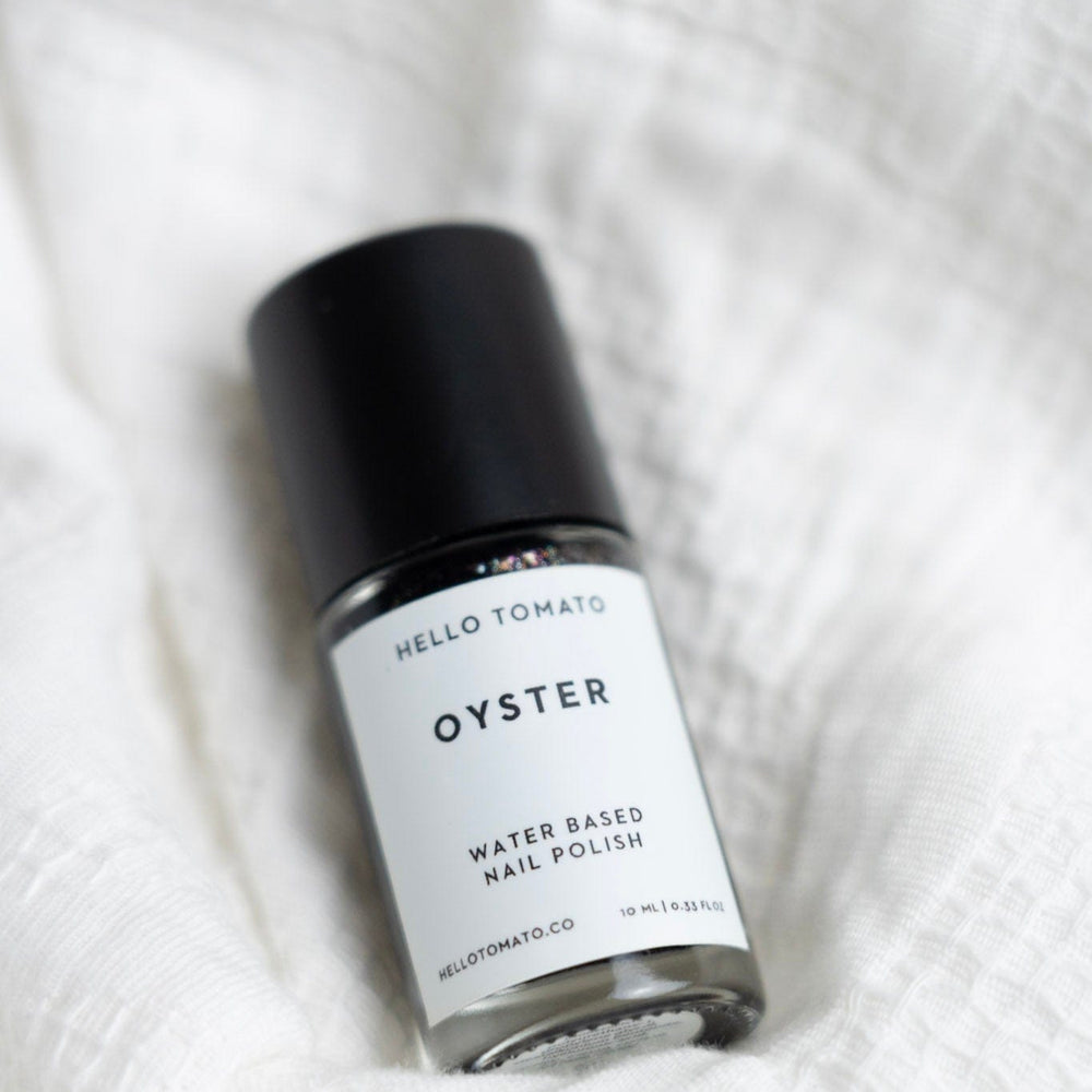 Bottle of 'Oyster' water-based nail polish by Hello Tomato on a white fabric background
