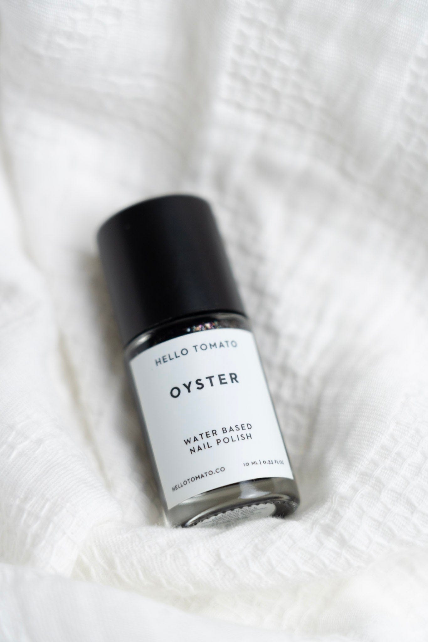 Bottle of 'Oyster' water-based nail polish by Hello Tomato on a white fabric background