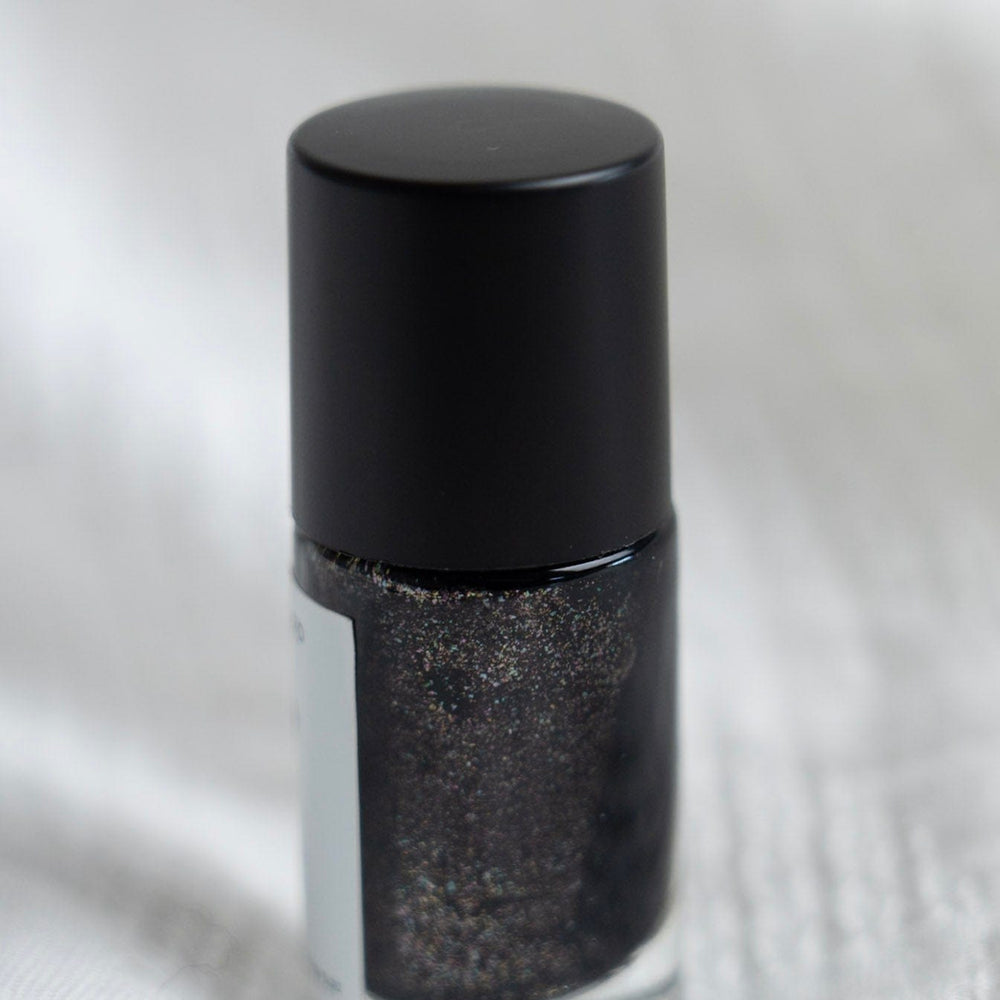 Black nail polish bottle with glittery black polish on a textured white background