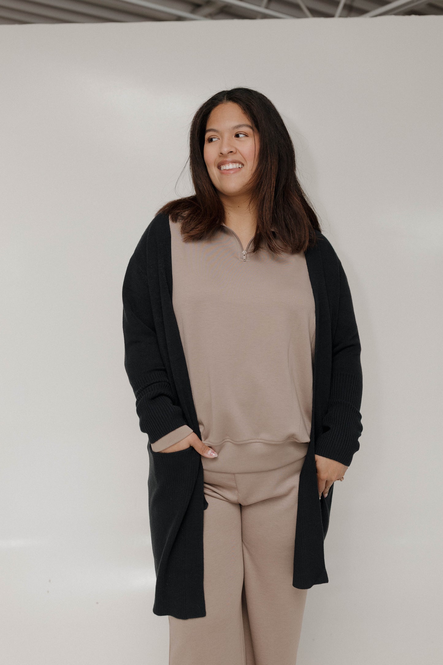 Woman wearing a beige outfit with a black cardigan against a white background