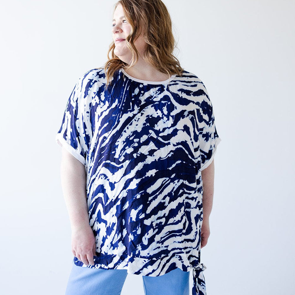 A person with long hair wearing a light blue and white PATTERN CHIFFON BLOUSE WITH KNIT BACK by Love Marlow and light blue pants stands against a plain white background.