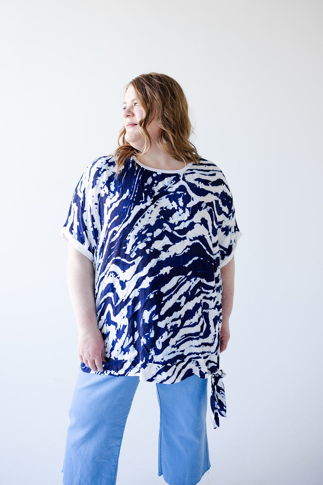 A person with long hair wearing a light blue and white PATTERN CHIFFON BLOUSE WITH KNIT BACK by Love Marlow and light blue pants stands against a plain white background.