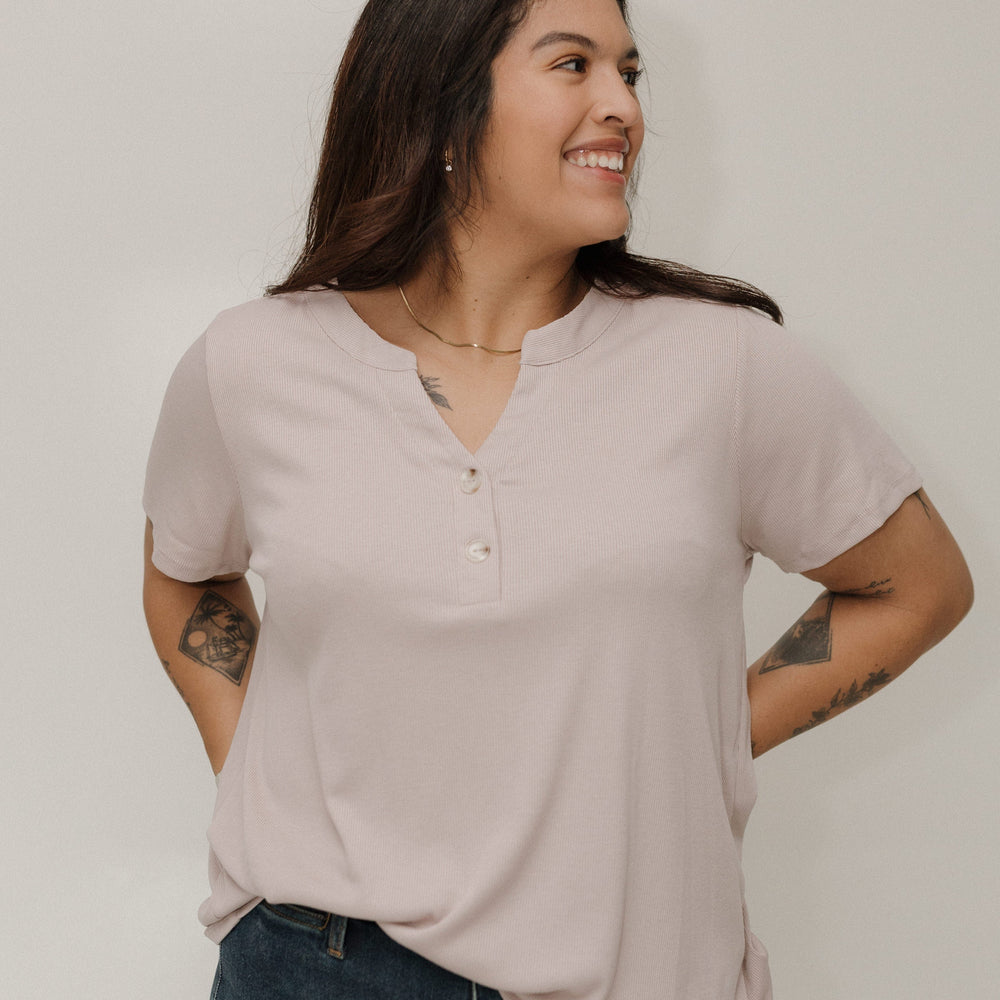 Woman wearing a pearl henley shirt and blue jeans against a white background