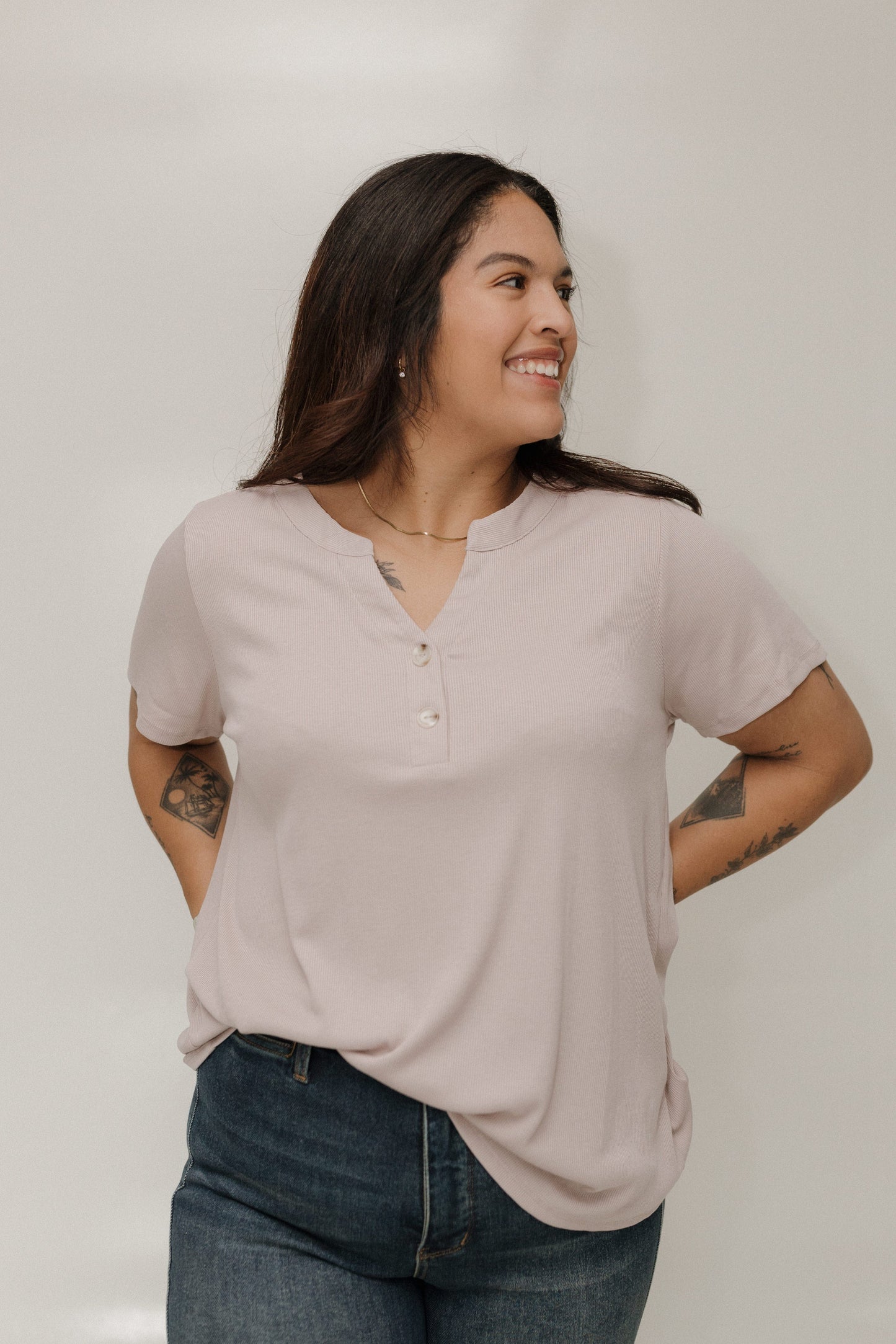 Woman wearing a pearl henley shirt and blue jeans against a white background