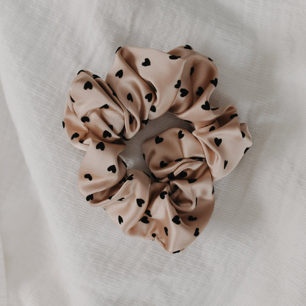 pink scrunchie with black heart patterns on a white fabric background