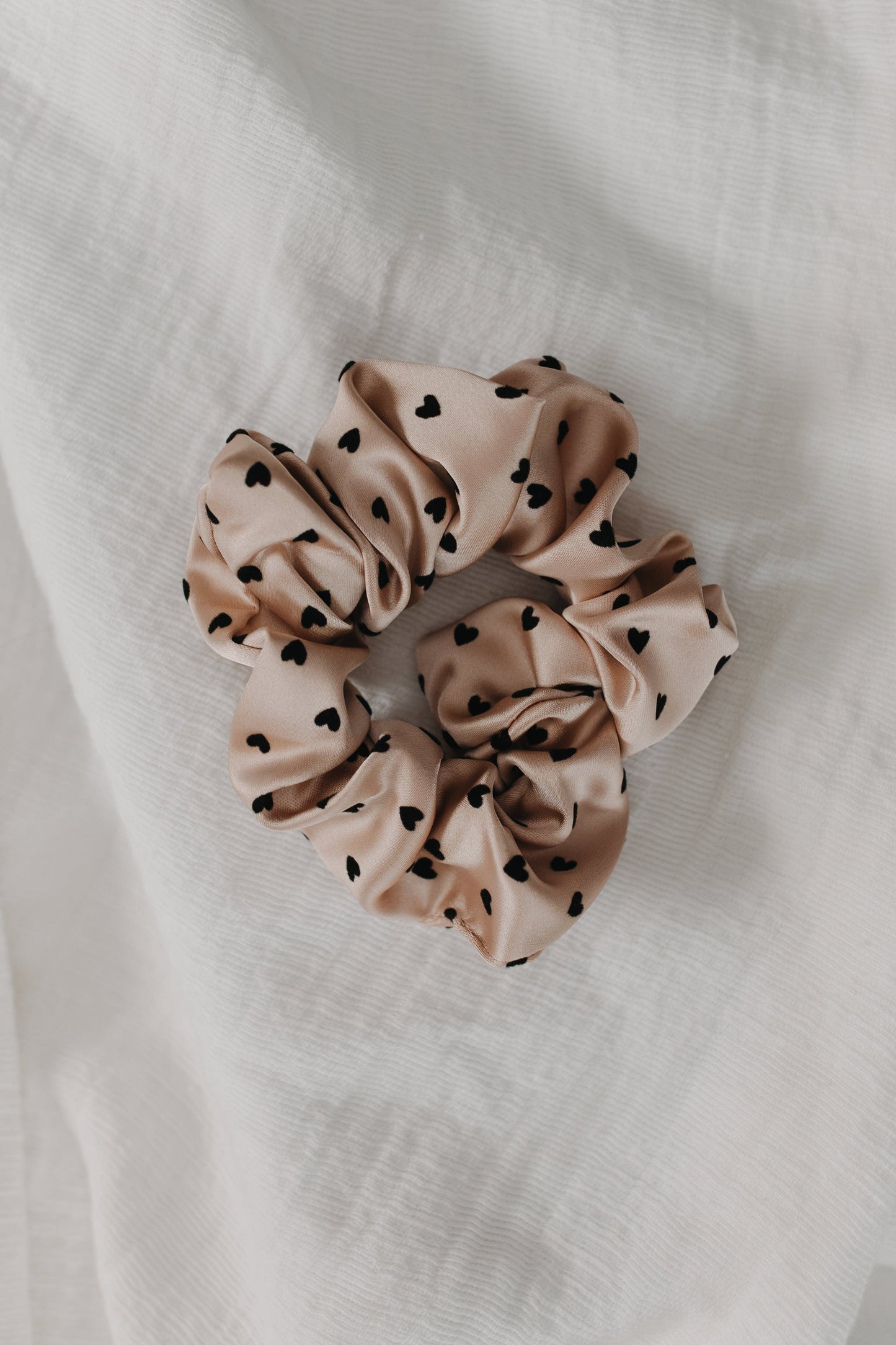 pink scrunchie with black heart patterns on a white fabric background