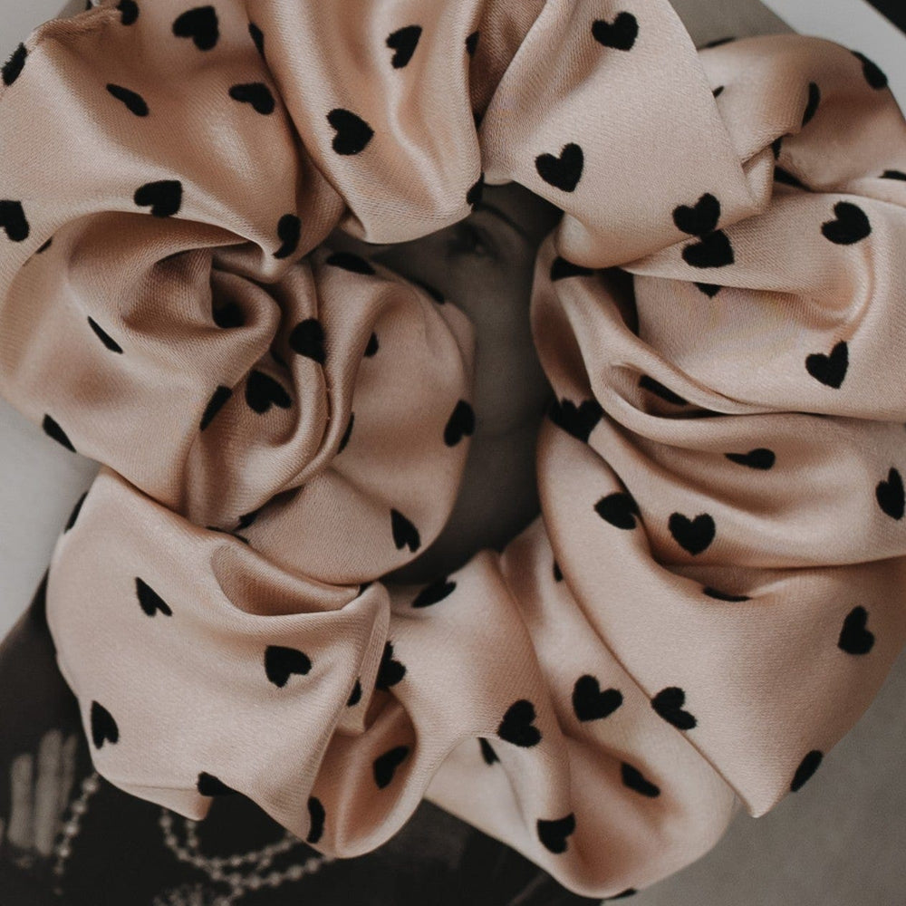 Pink scrunchie with black heart patterns on a neutral background