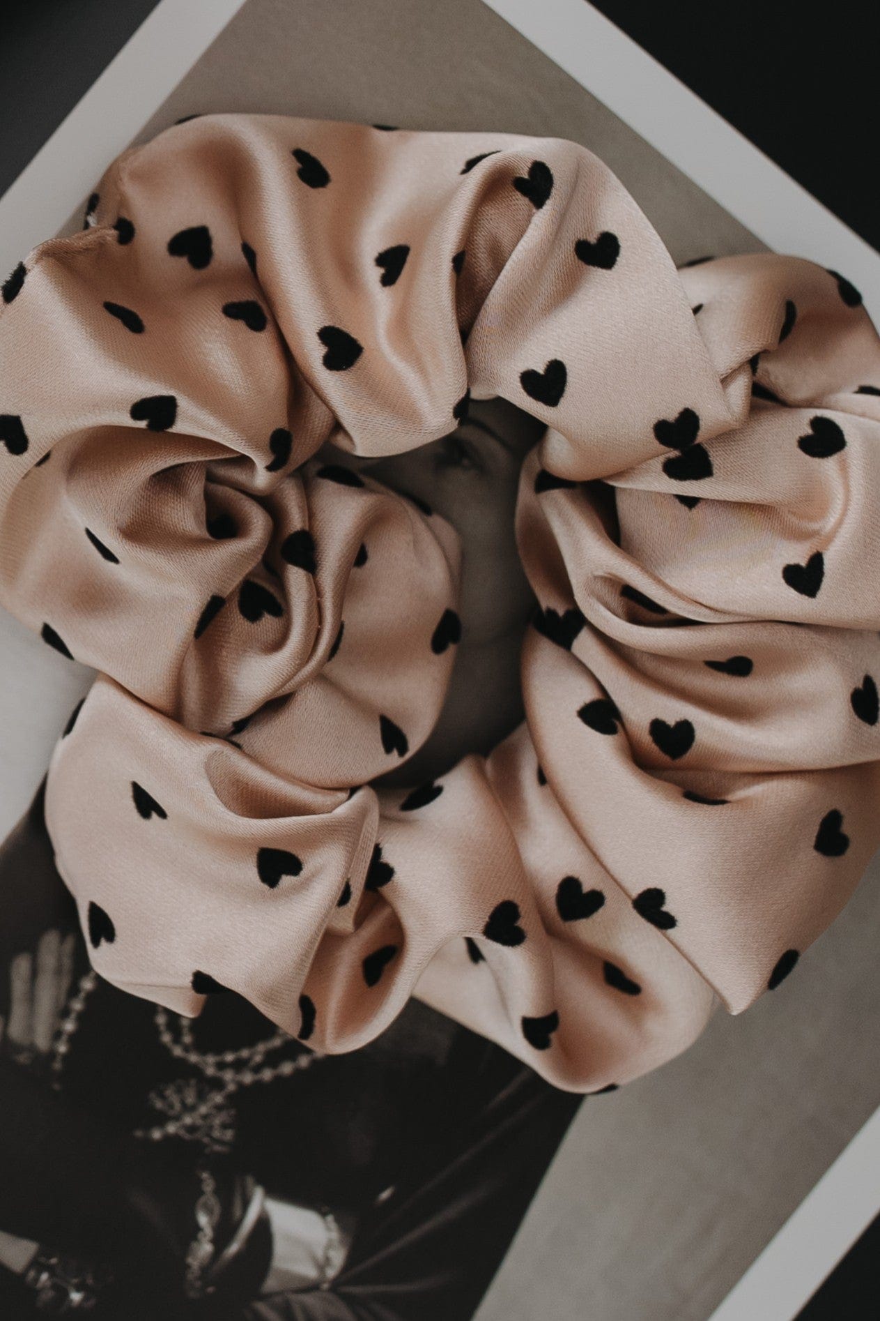 Pink scrunchie with black heart patterns on a neutral background