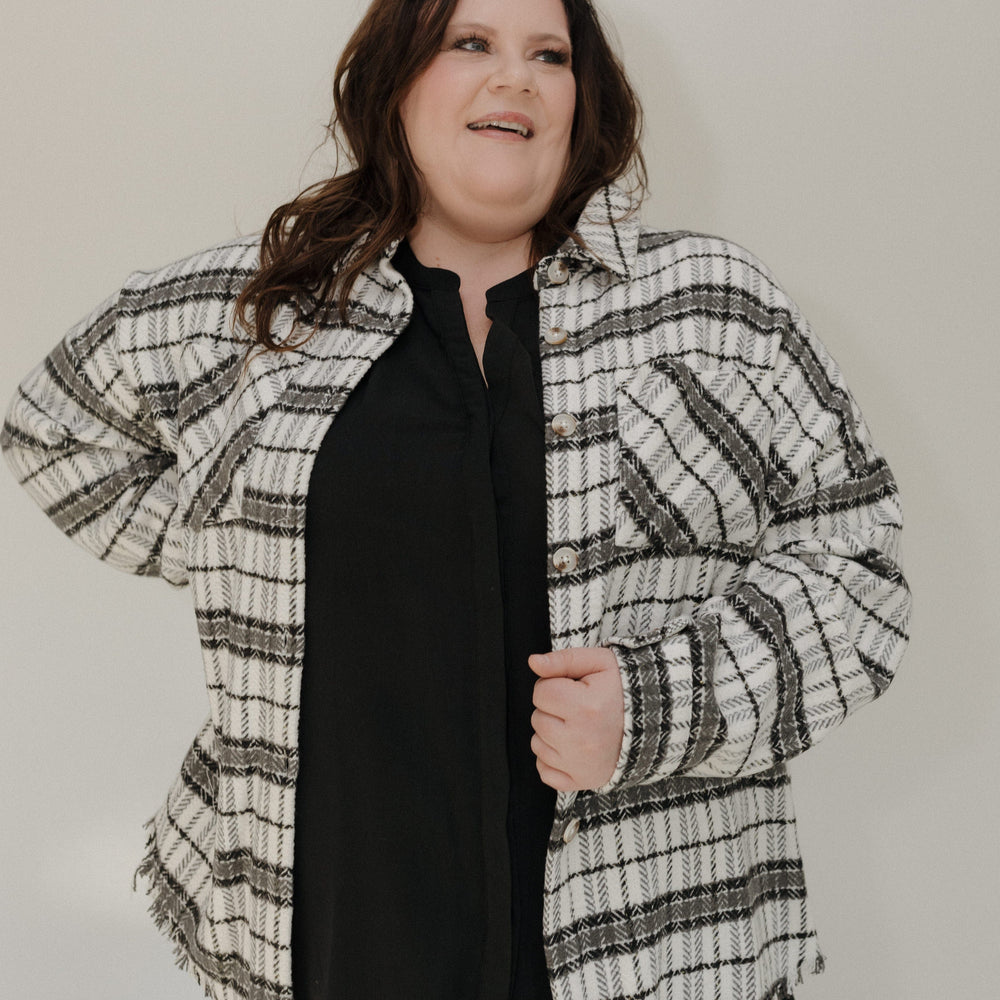 Person wearing a plaid shirt over a black top against a plain background