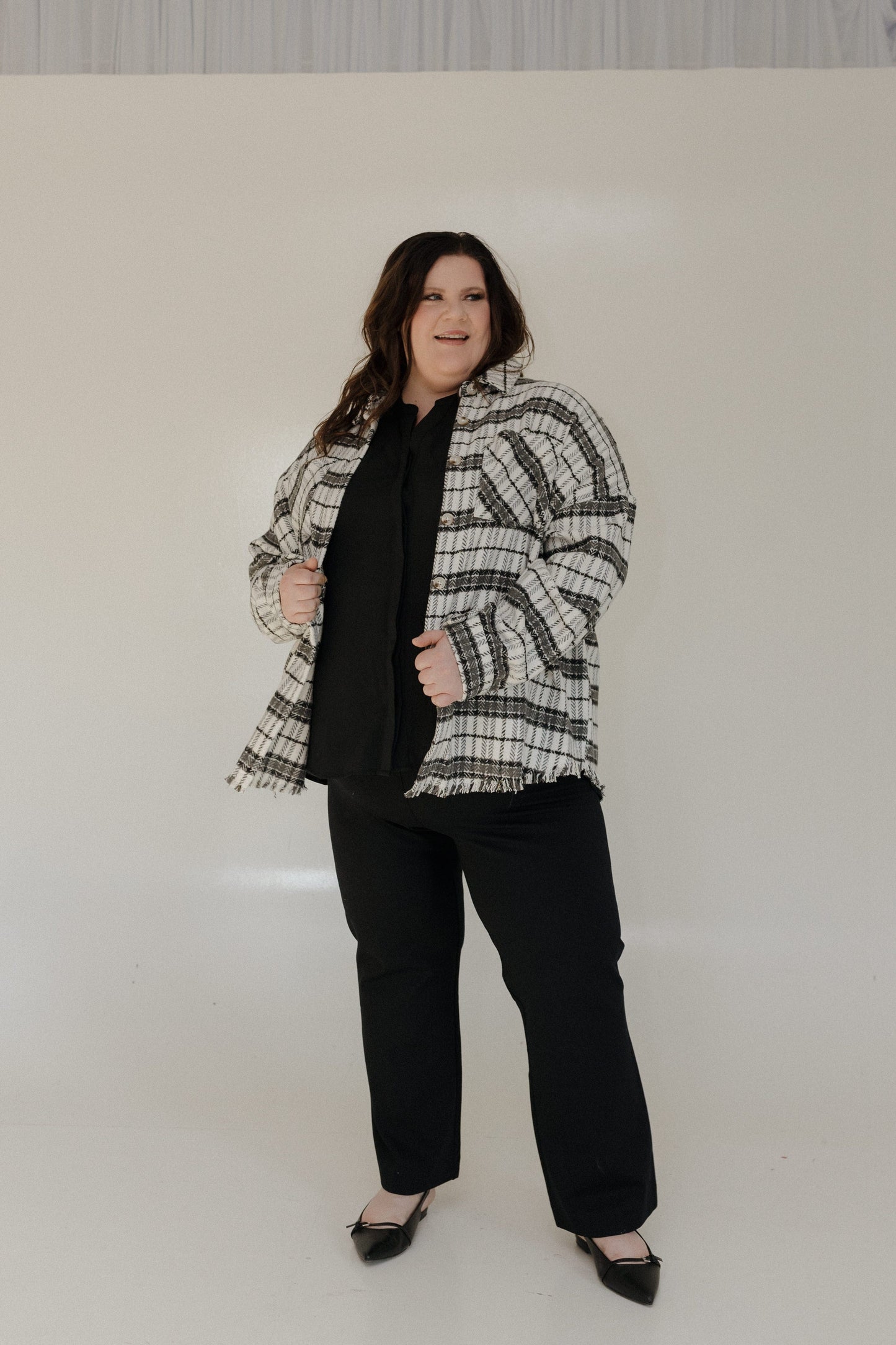 Person wearing a checkered jacket over a black top and pants on a white background