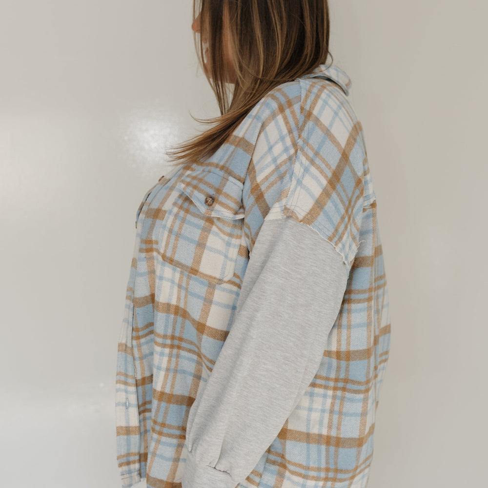 Person wearing a plaid shirt over a gray sweater against a plain background