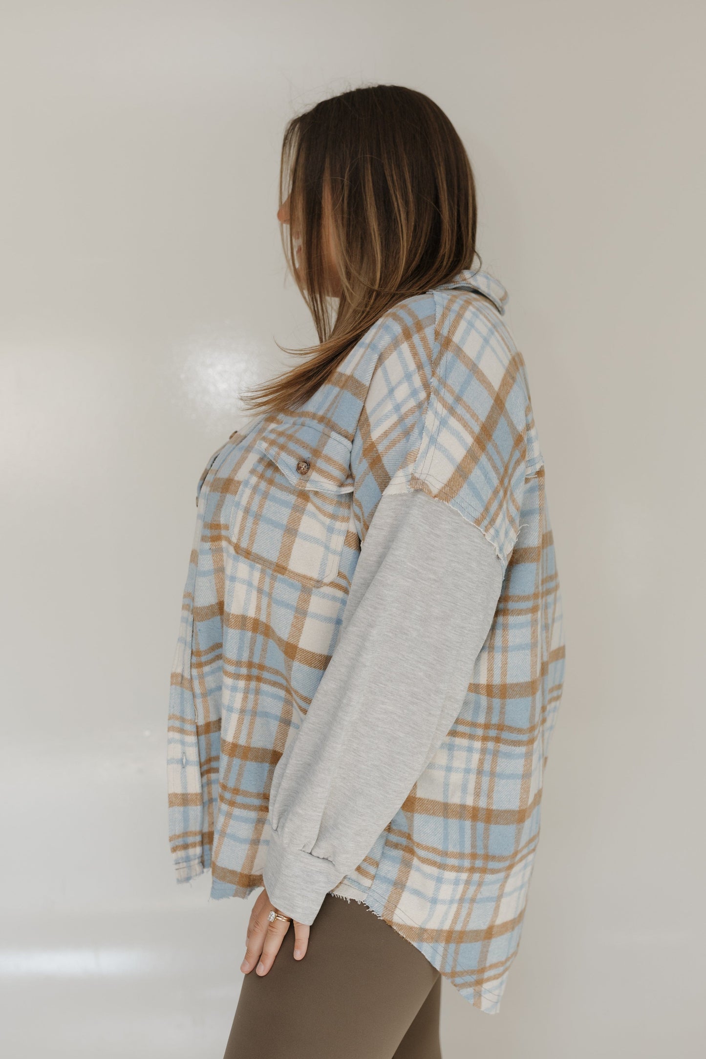 Person wearing a plaid shirt over a gray sweater against a plain background