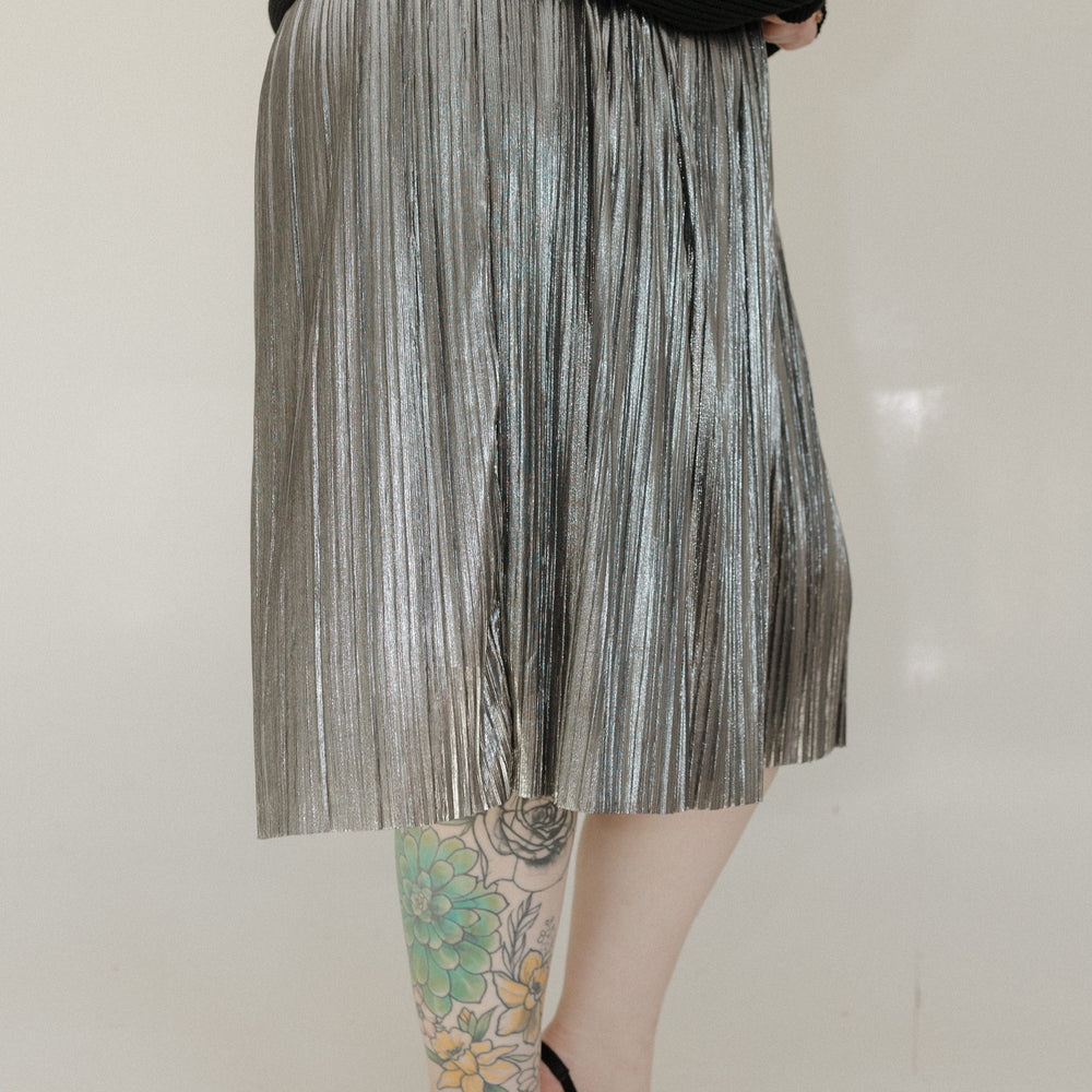 Person wearing a pleated skirt and black shoes on a plain background