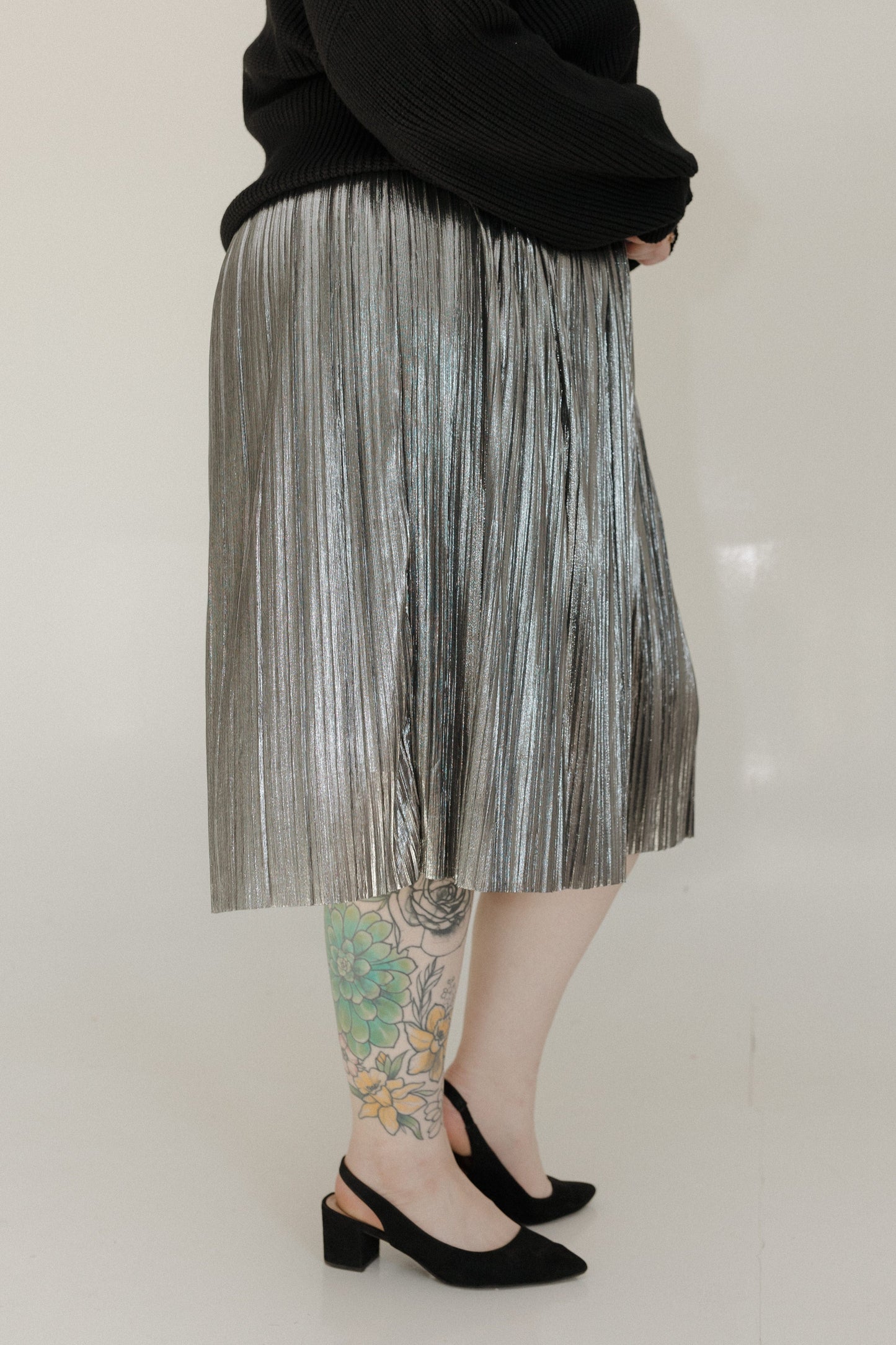 Person wearing a pleated skirt and black shoes on a plain background