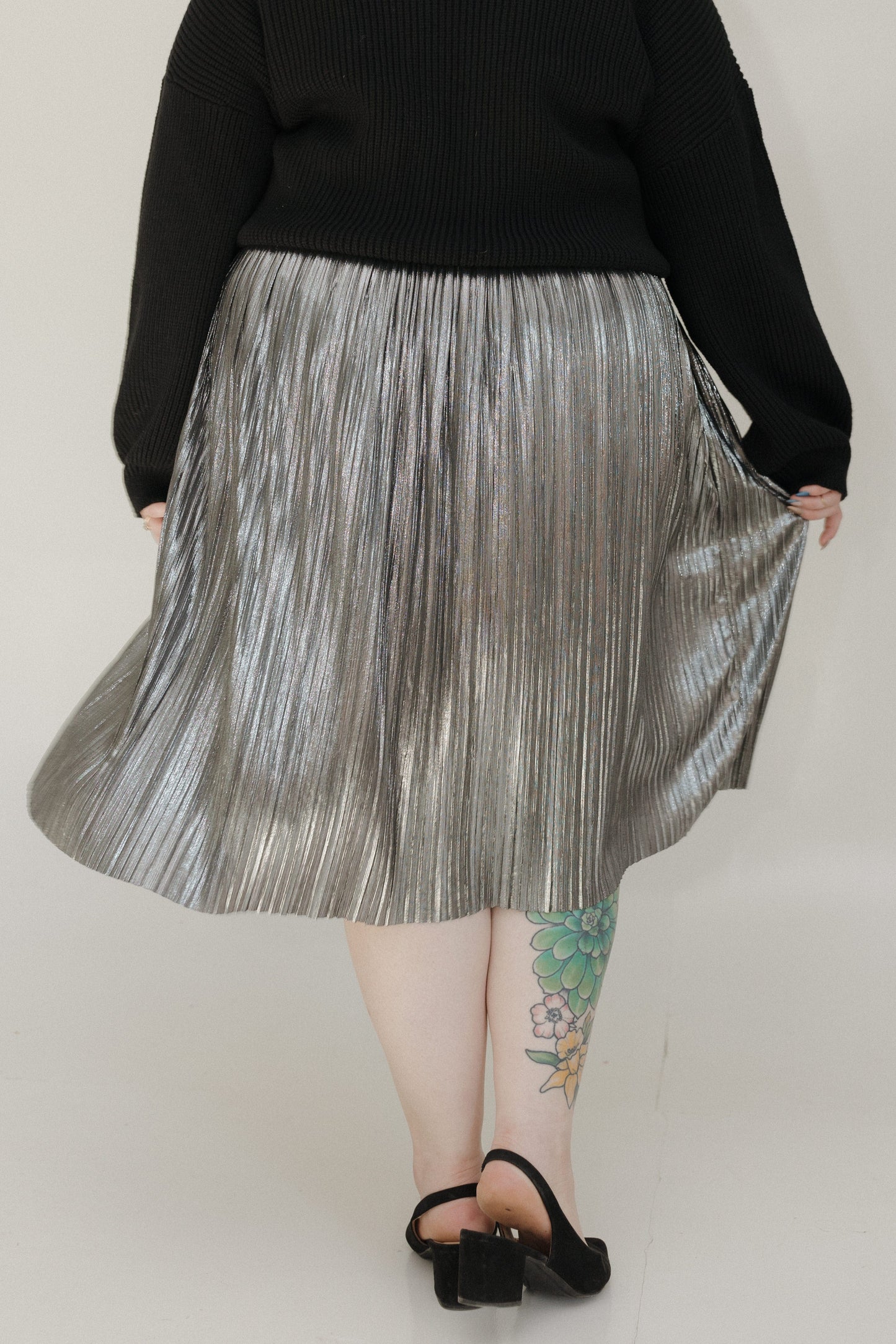 Person wearing a black sweater and silver pleated skirt on a plain background