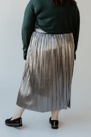 A person in a green top and metallic silver pleated midi skirt stands with their back to the camera, showcasing a stylish plus-size ensemble.