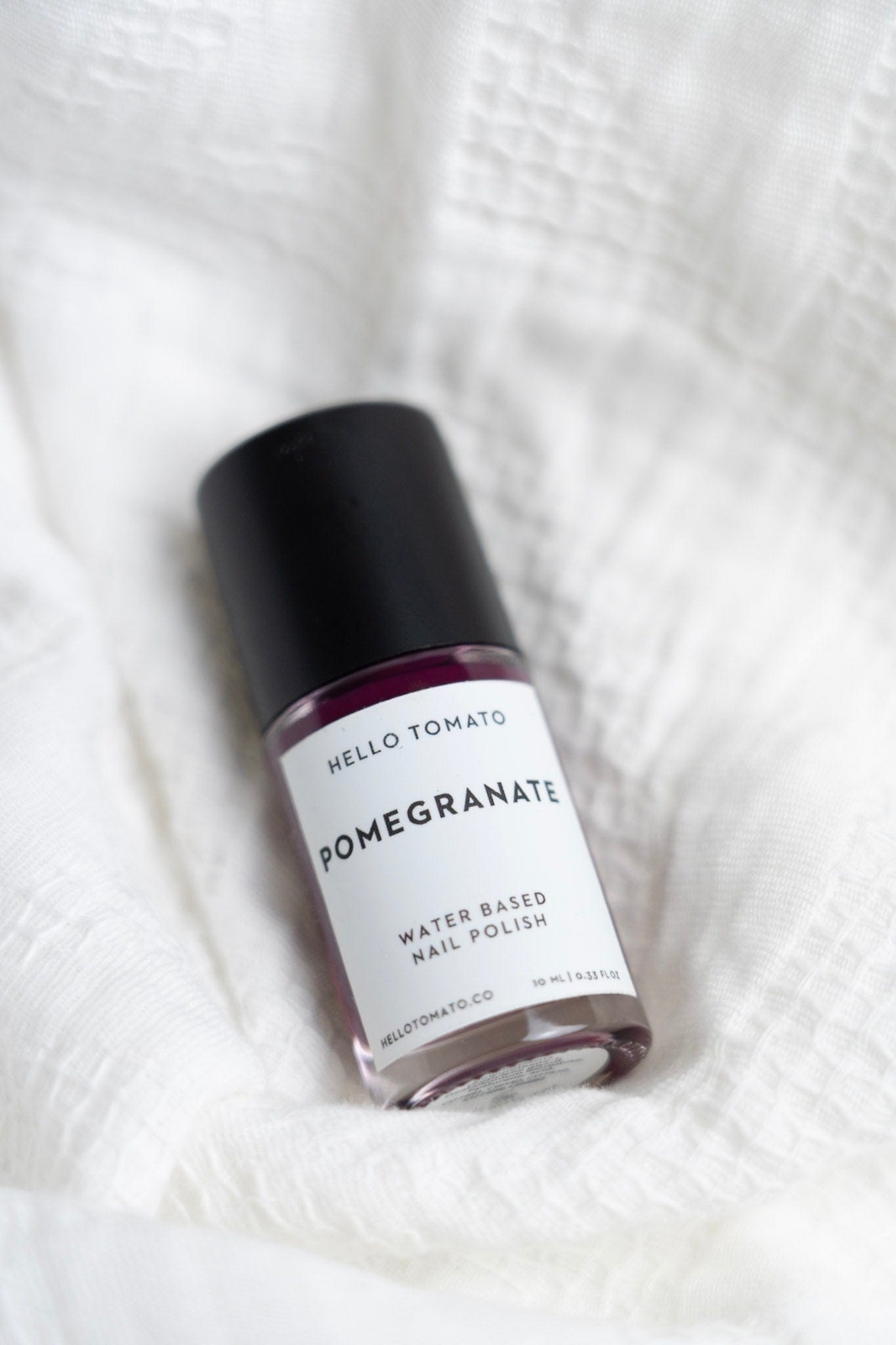 Bottle of Hello Tomato pomegranate water-based nail polish on a white fabric background