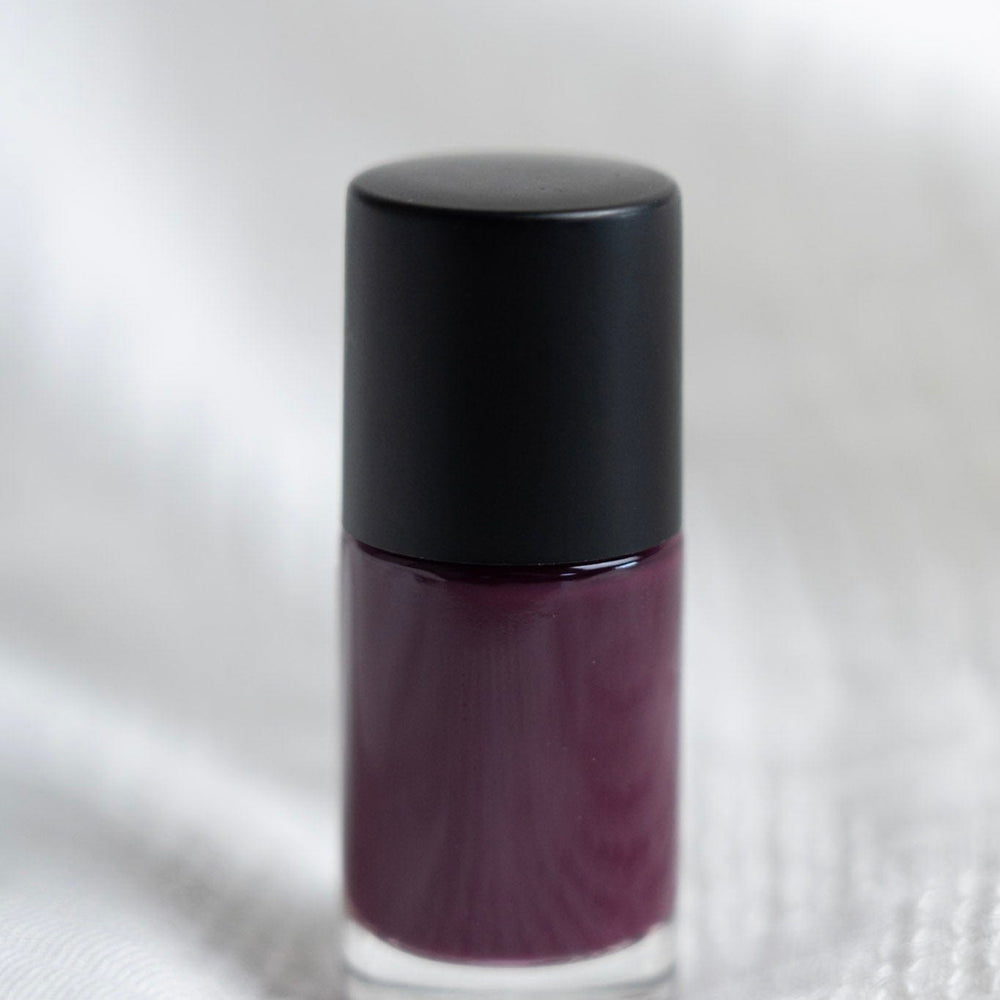 Purple nail polish bottle with black cap on a white textured background