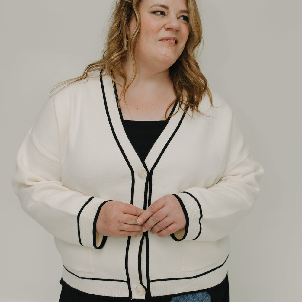 Woman wearing a white cardigan with black trim against a plain background