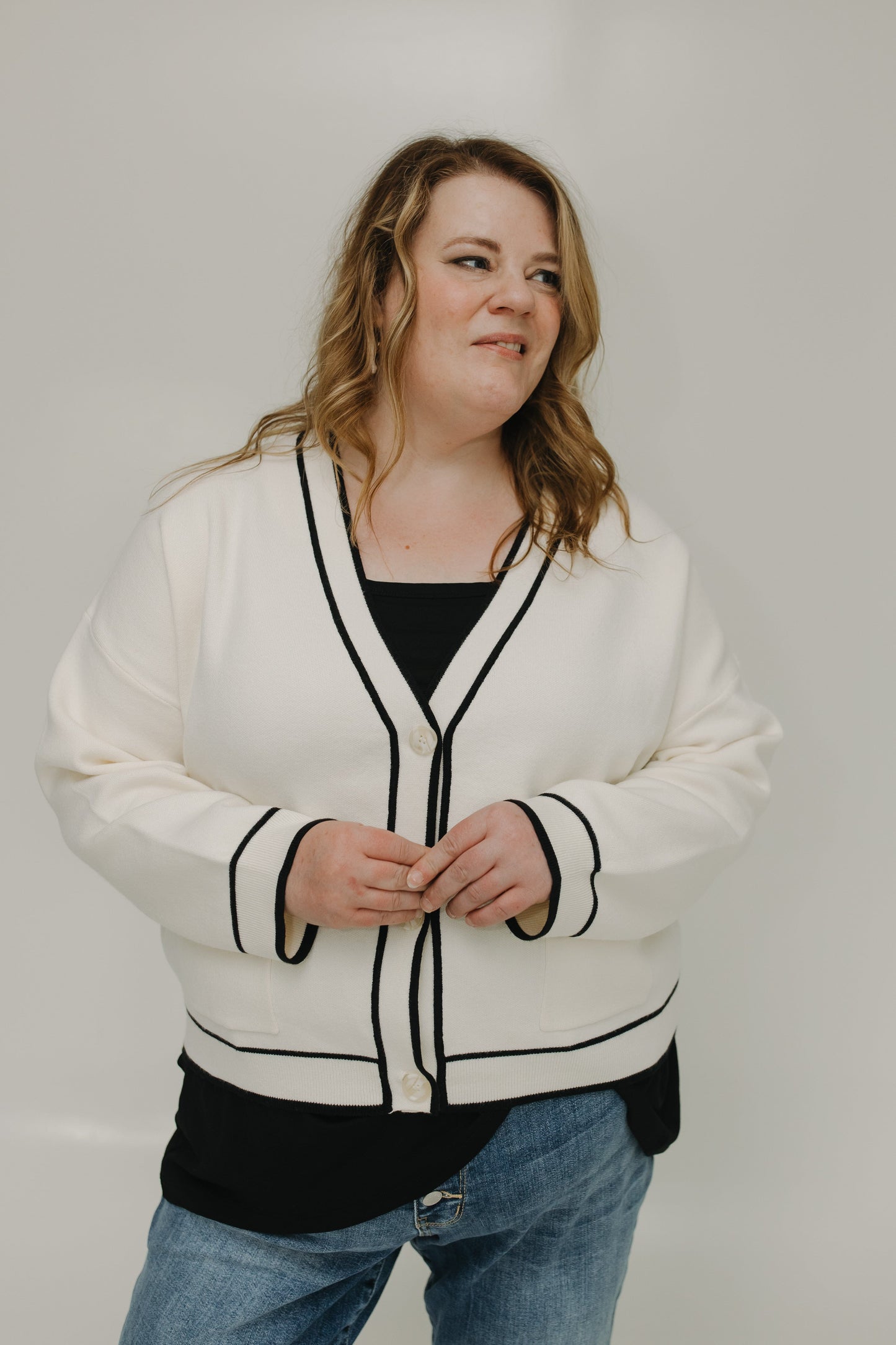Woman wearing a white cardigan with black trim against a plain background