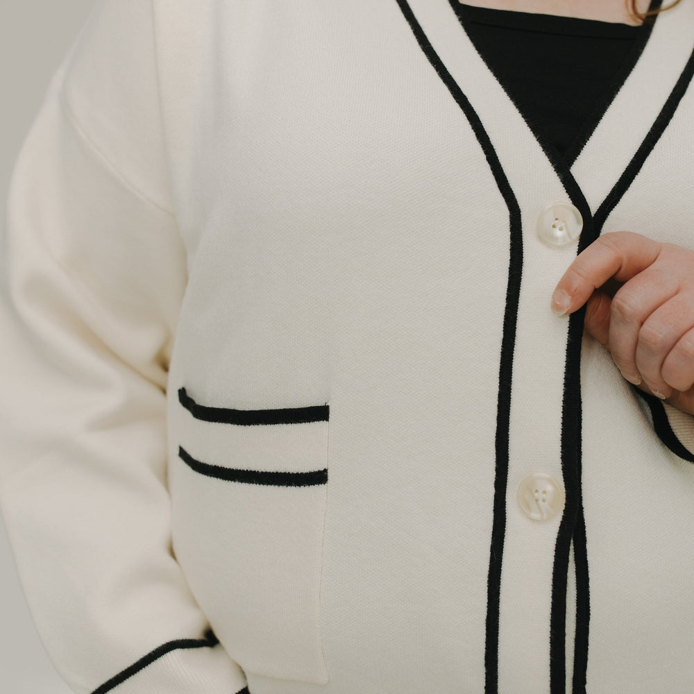 White cardigan with black trim worn by a person on a neutral background