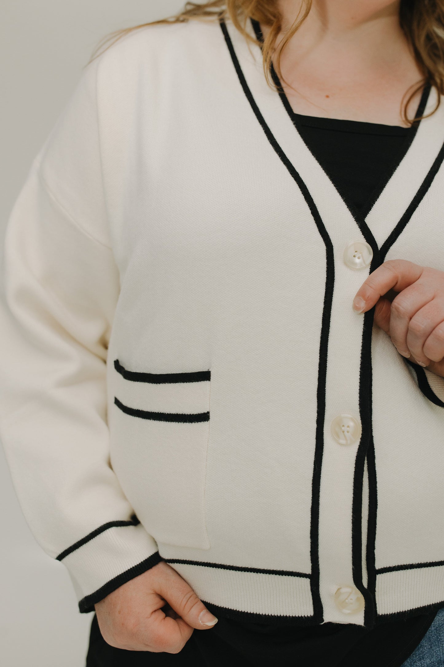 White cardigan with black trim worn by a person on a neutral background