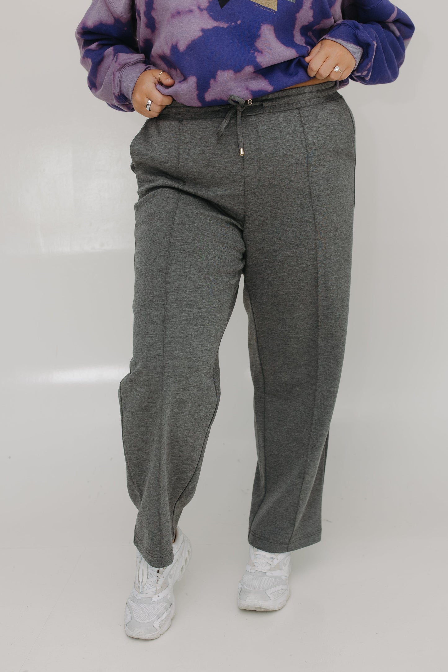 Person wearing gray sweatpants and a purple tie-dye hoodie on a white background