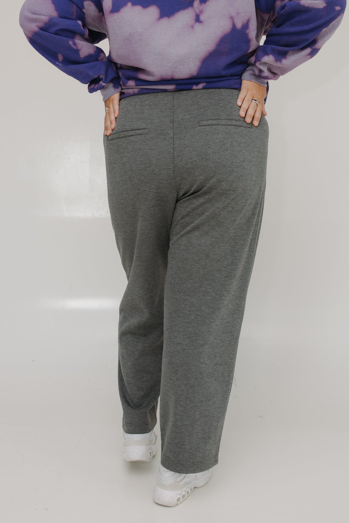 Person wearing a purple and blue tie-dye sweater and gray sweatpants on a white background