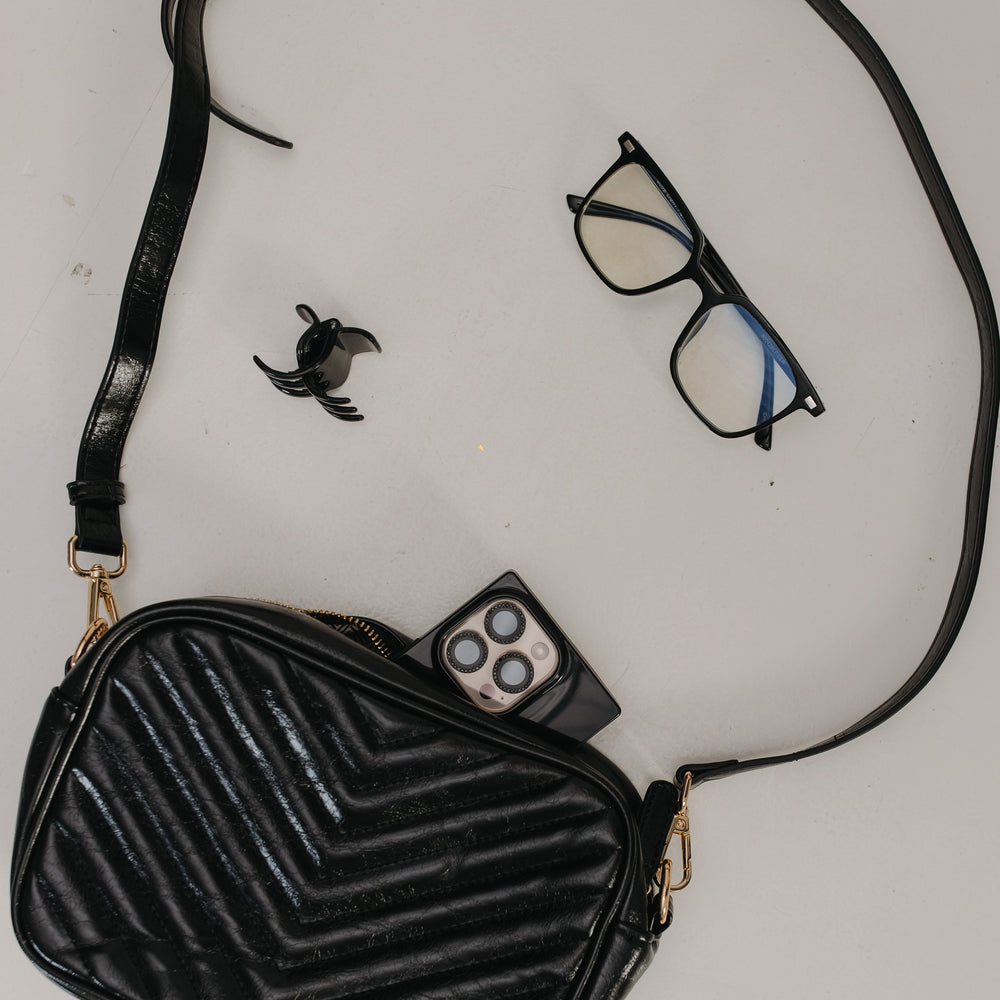 Black textured handbag with a strap, glasses, remote control, and small bird figurine on a light gray background.