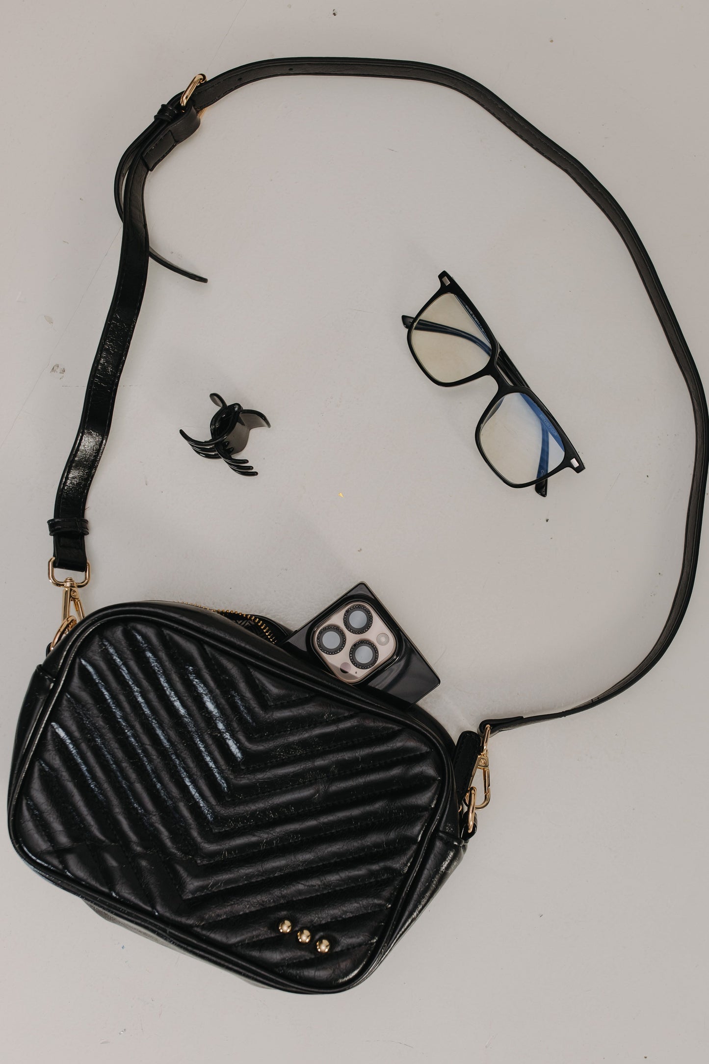 Black textured handbag with a strap, glasses, remote control, and small bird figurine on a light gray background.