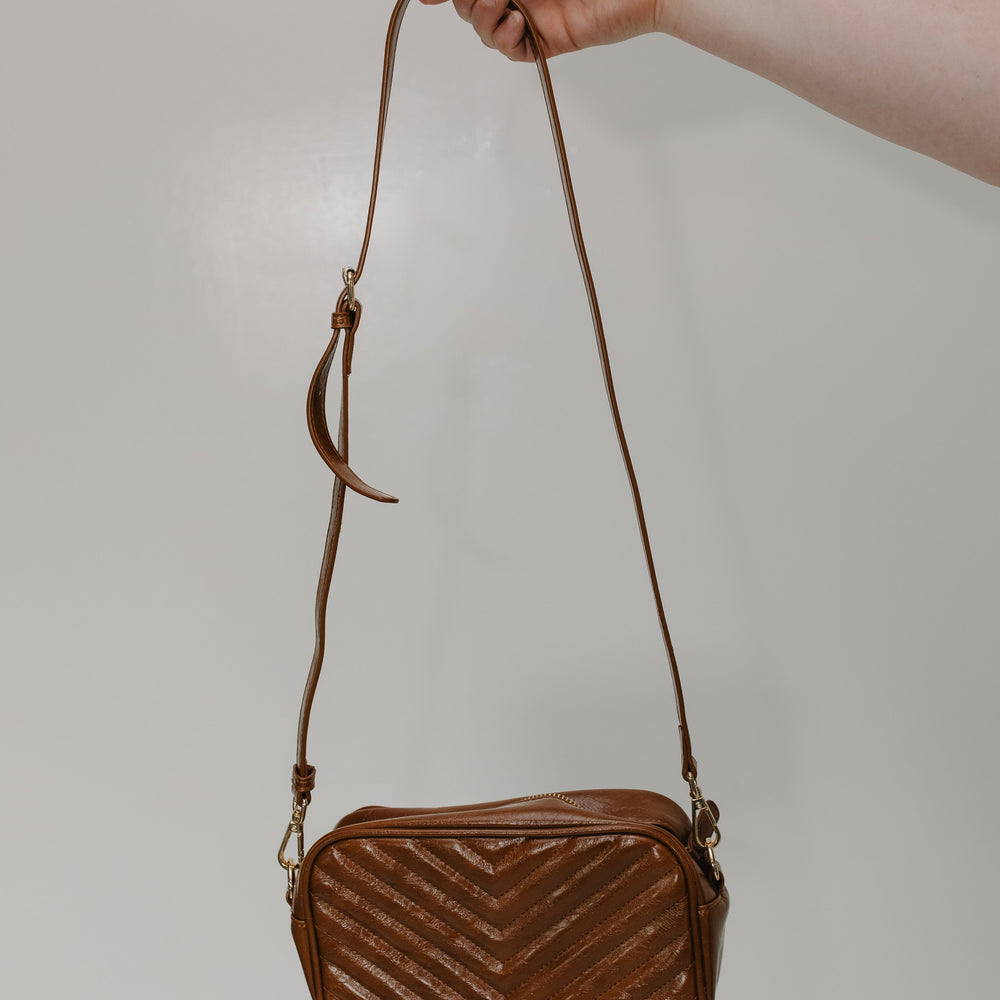 Brown quilted handbag held by a hand against a plain background