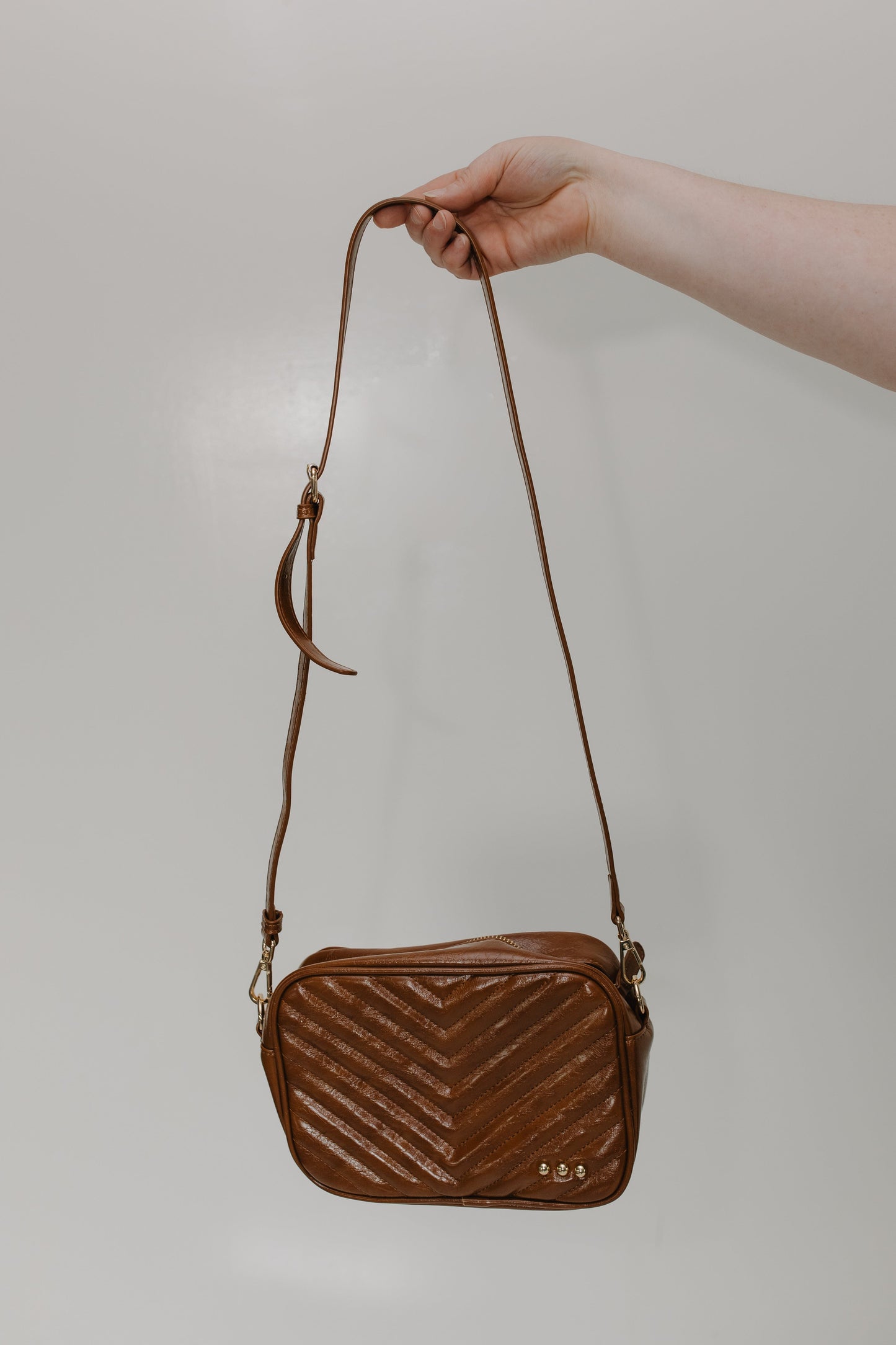 Brown quilted handbag held by a hand against a plain background