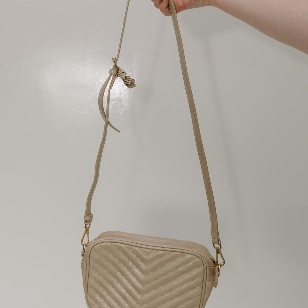 Sand crossbody bag held by a hand against a plain background