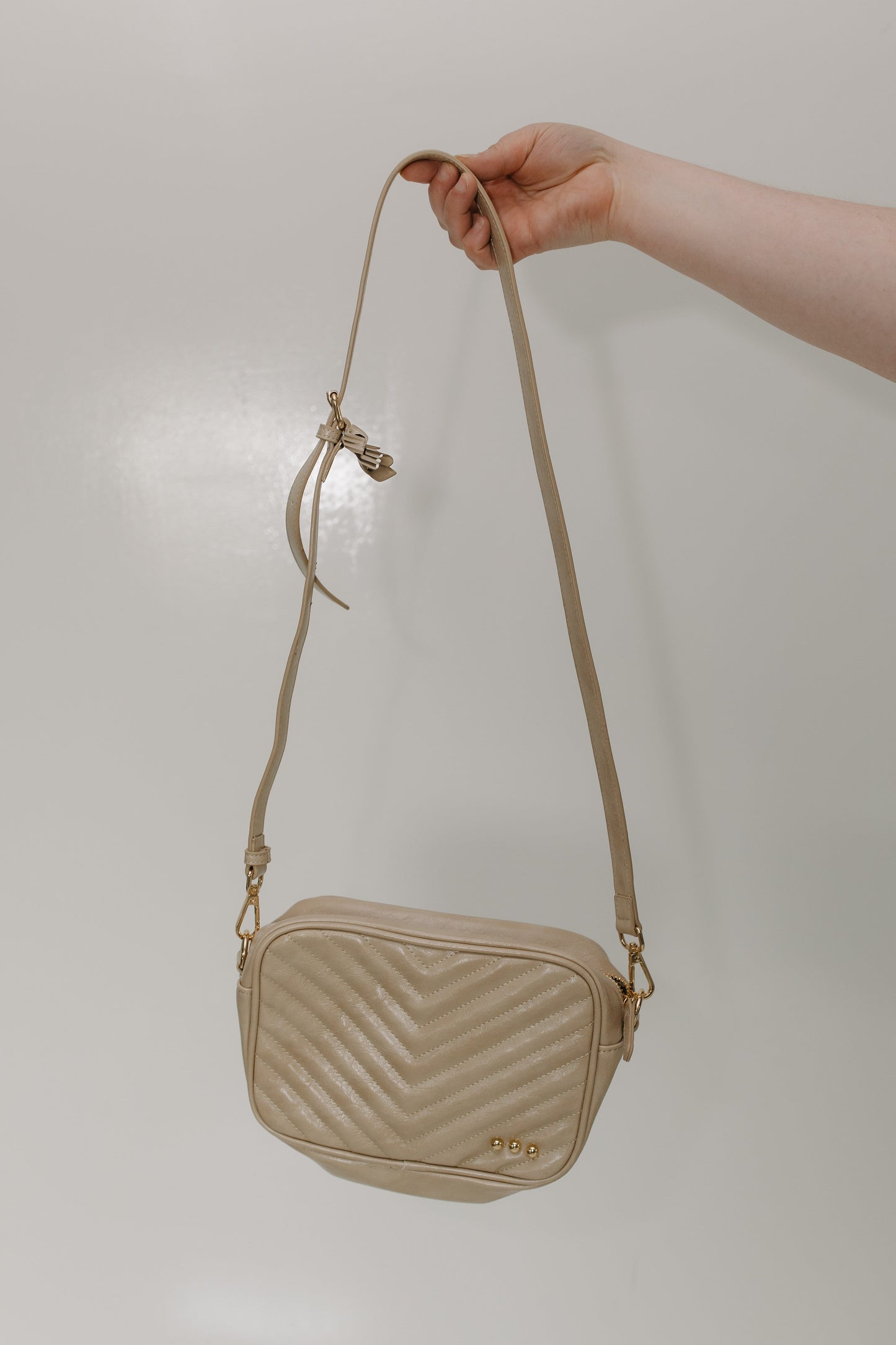 Sand crossbody bag held by a hand against a plain background