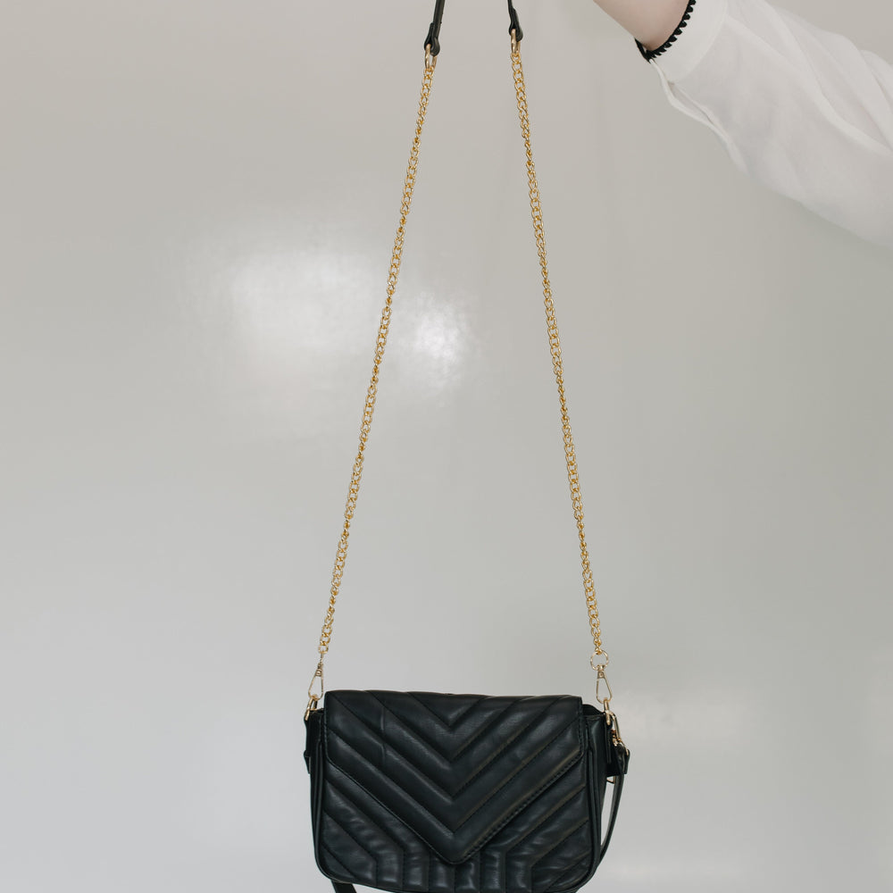 Black quilted handbag with a gold chain strap held by a person against a light gray background