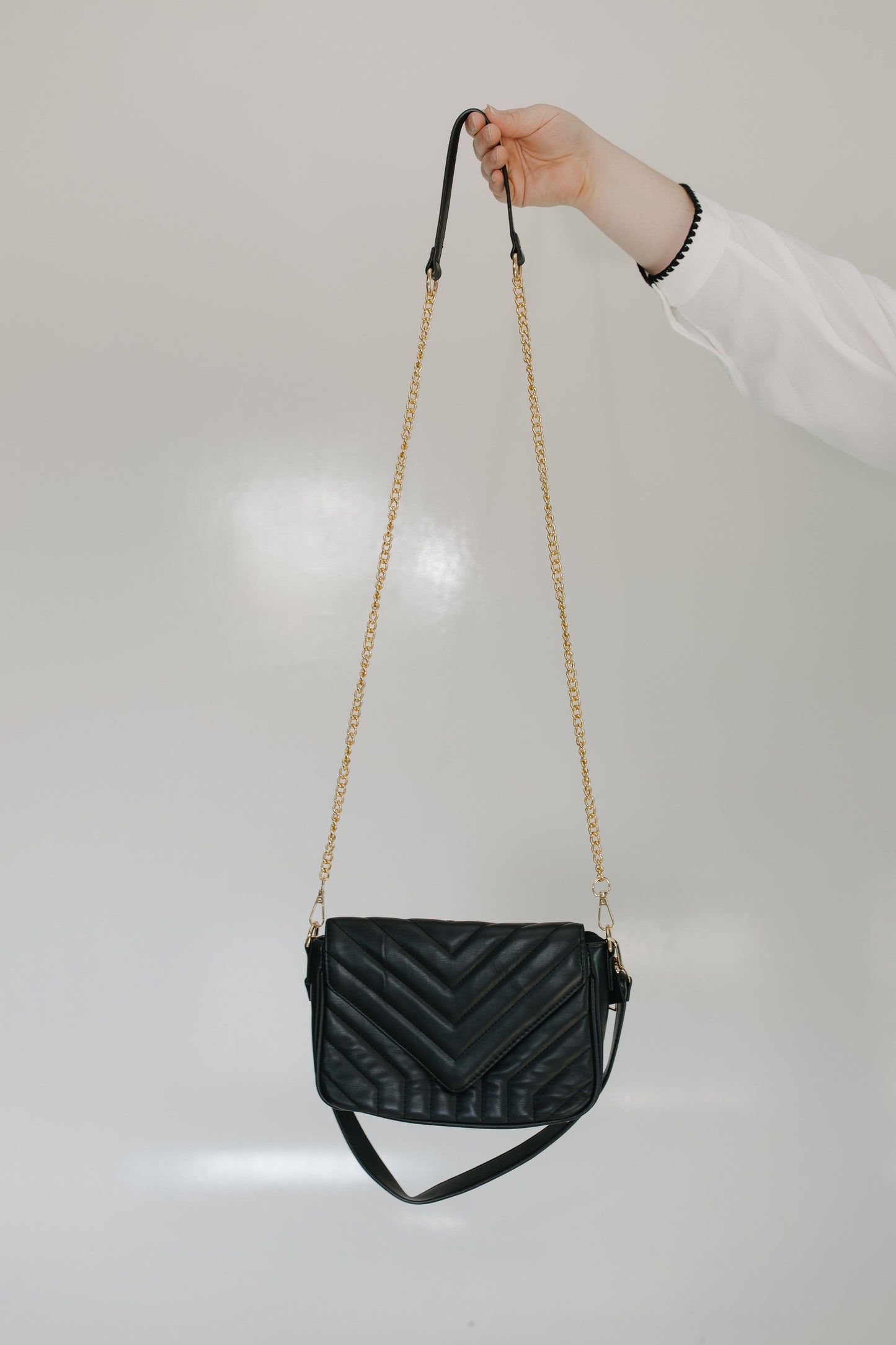Black quilted handbag with a gold chain strap held by a person against a light gray background